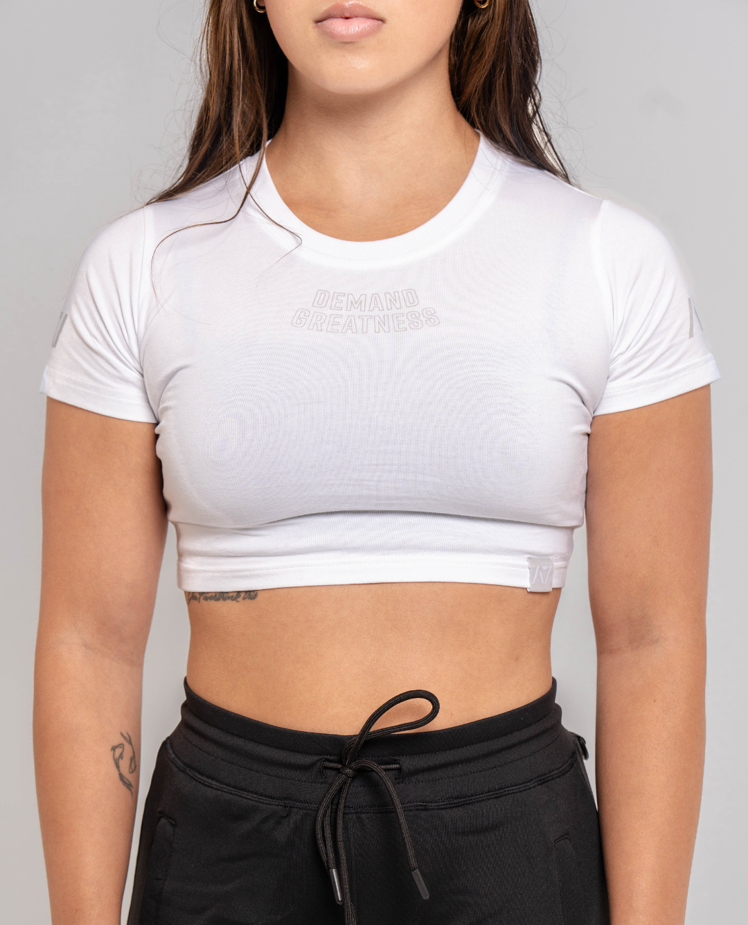 A woman wearing a white crop top with a Demand Greatness design on the upper chest and A7 logo on the upper back and sleeves.