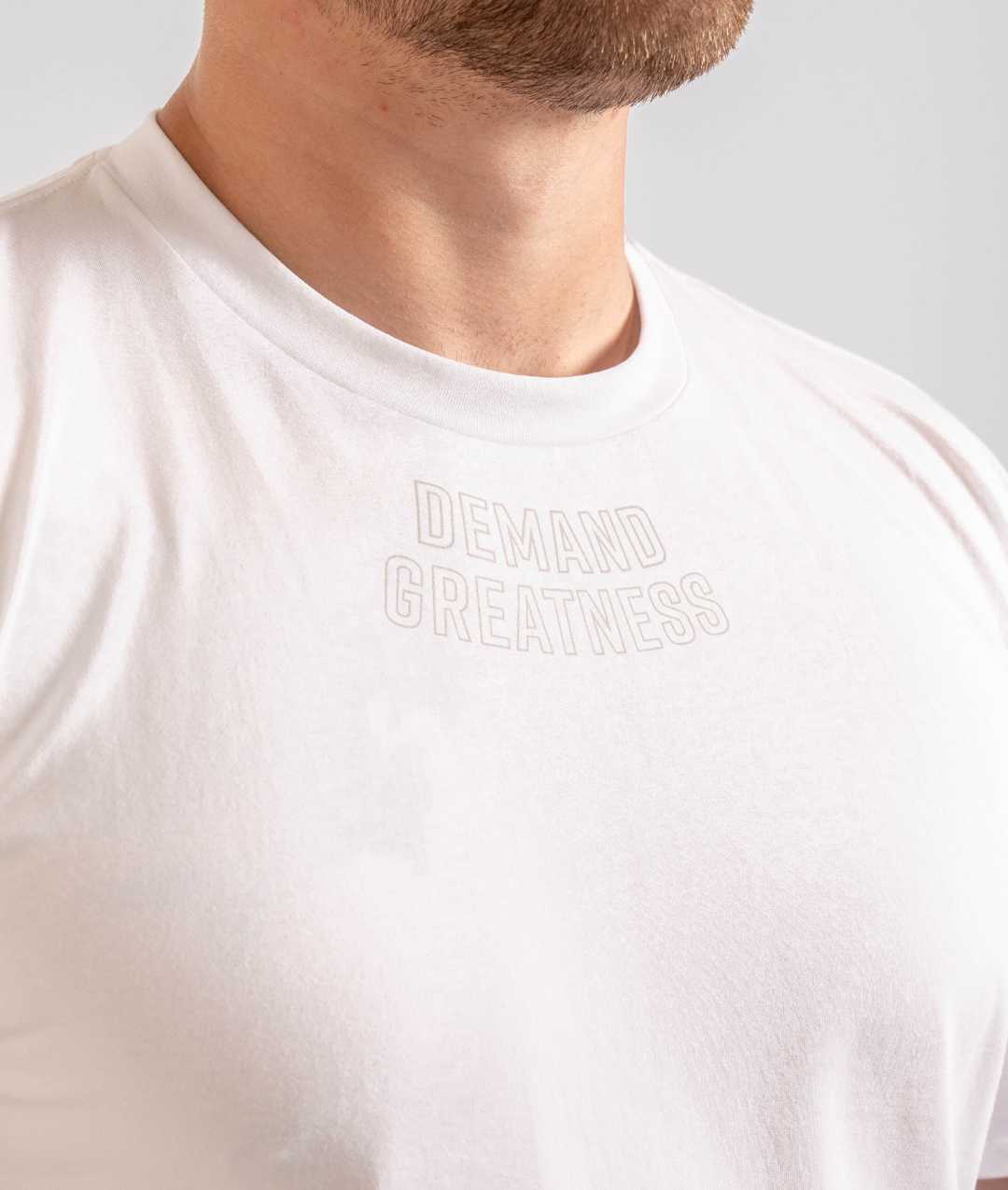 Close up of Demand Greatness text on the top of the chest on the front of the meet shirt
