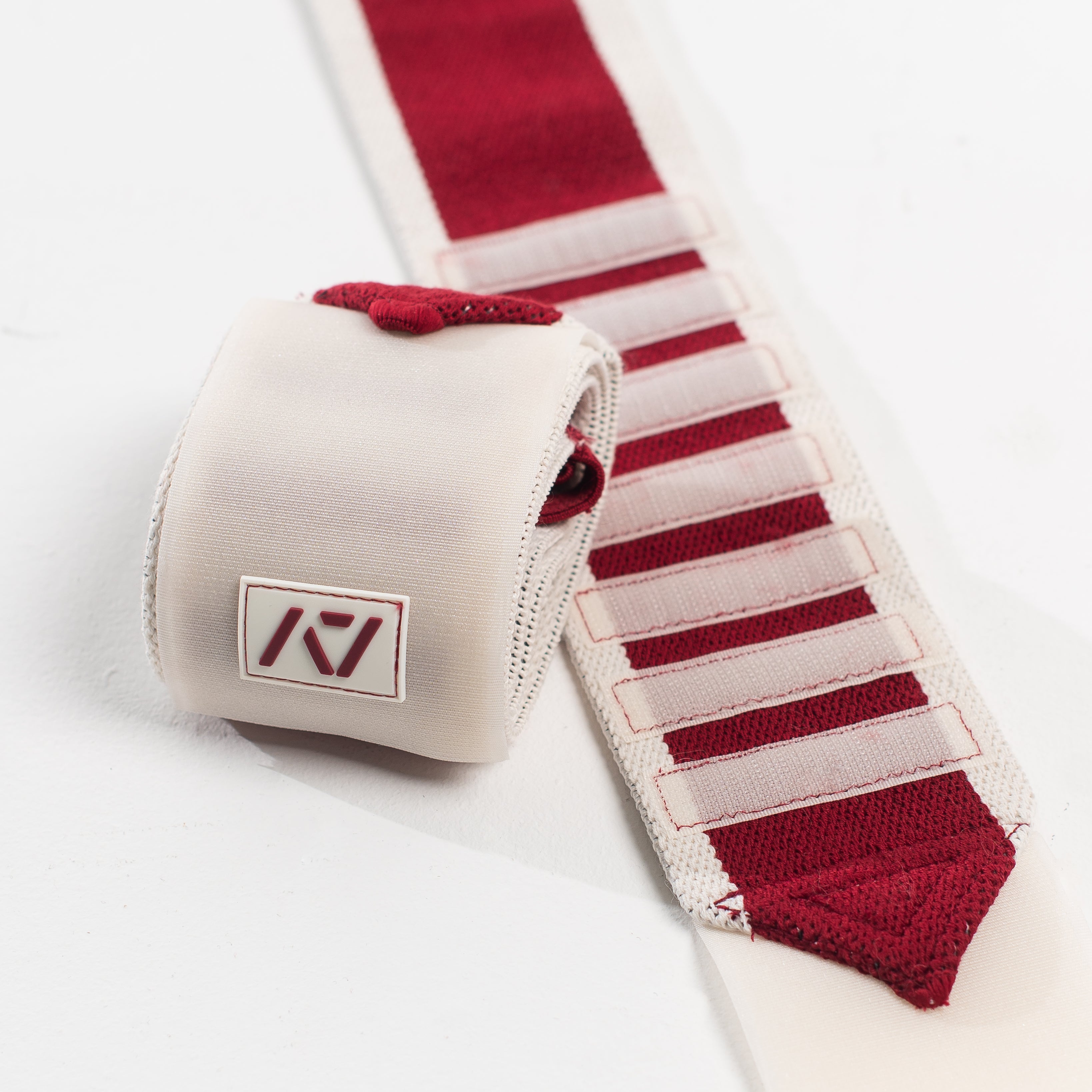 A pair of Zebra Wrist Wraps in red and white color with velcro strips and a silicone patch, designed for powerlifting.
