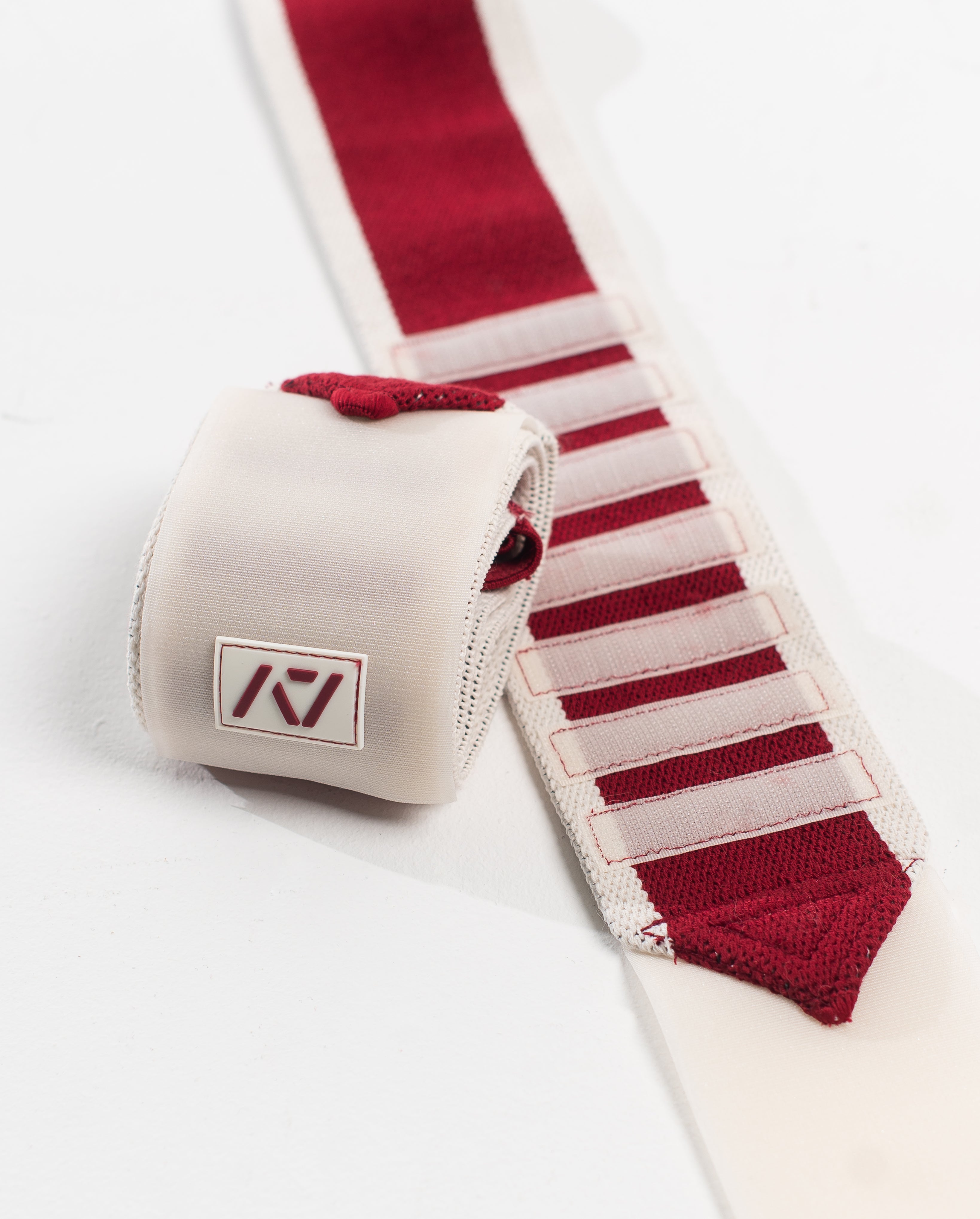 A pair of Zebra Wrist Wraps in red and white color with velcro strips and a silicone patch, designed for powerlifting.