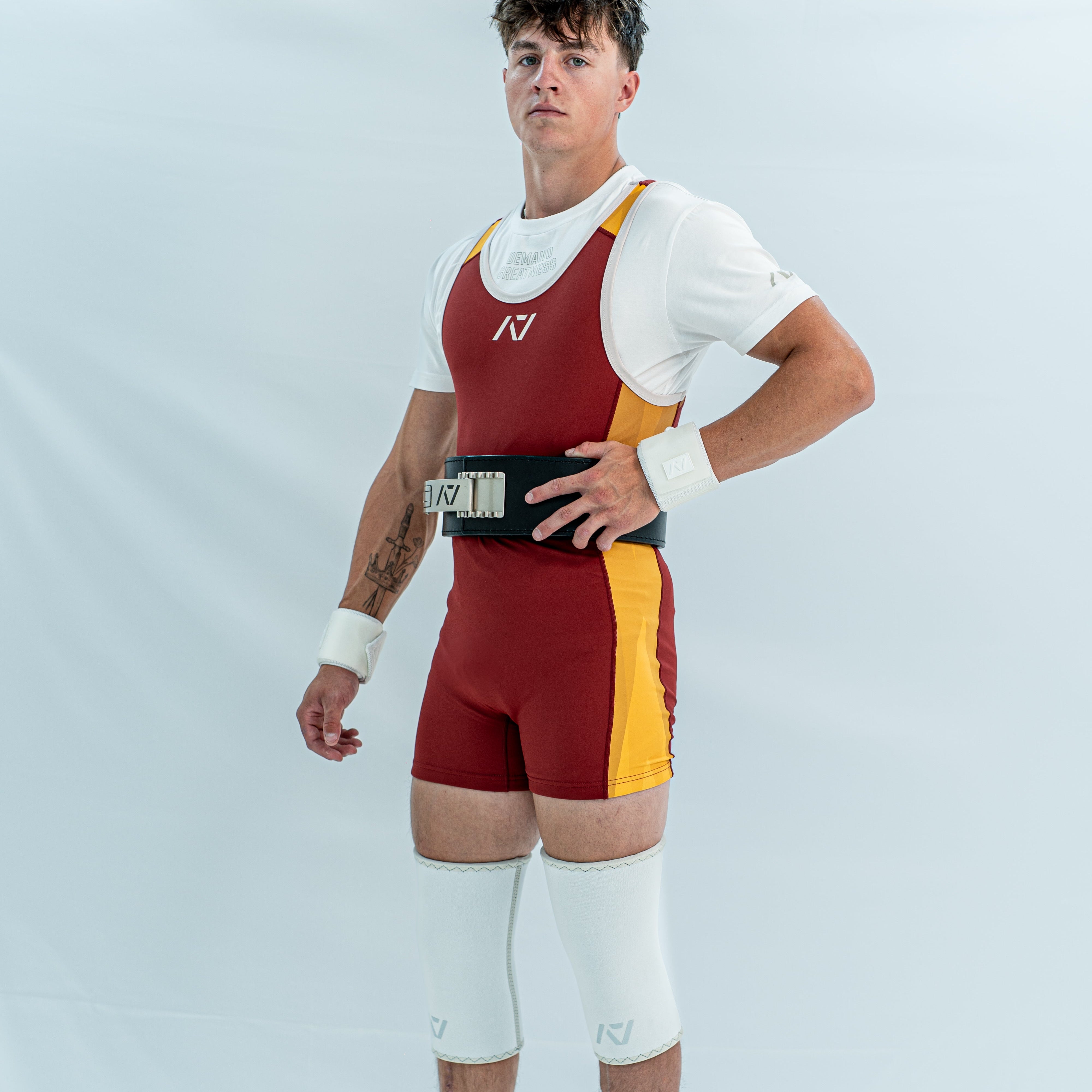 Male model wearing a maroon and yellow powerlifting singlet on a white background