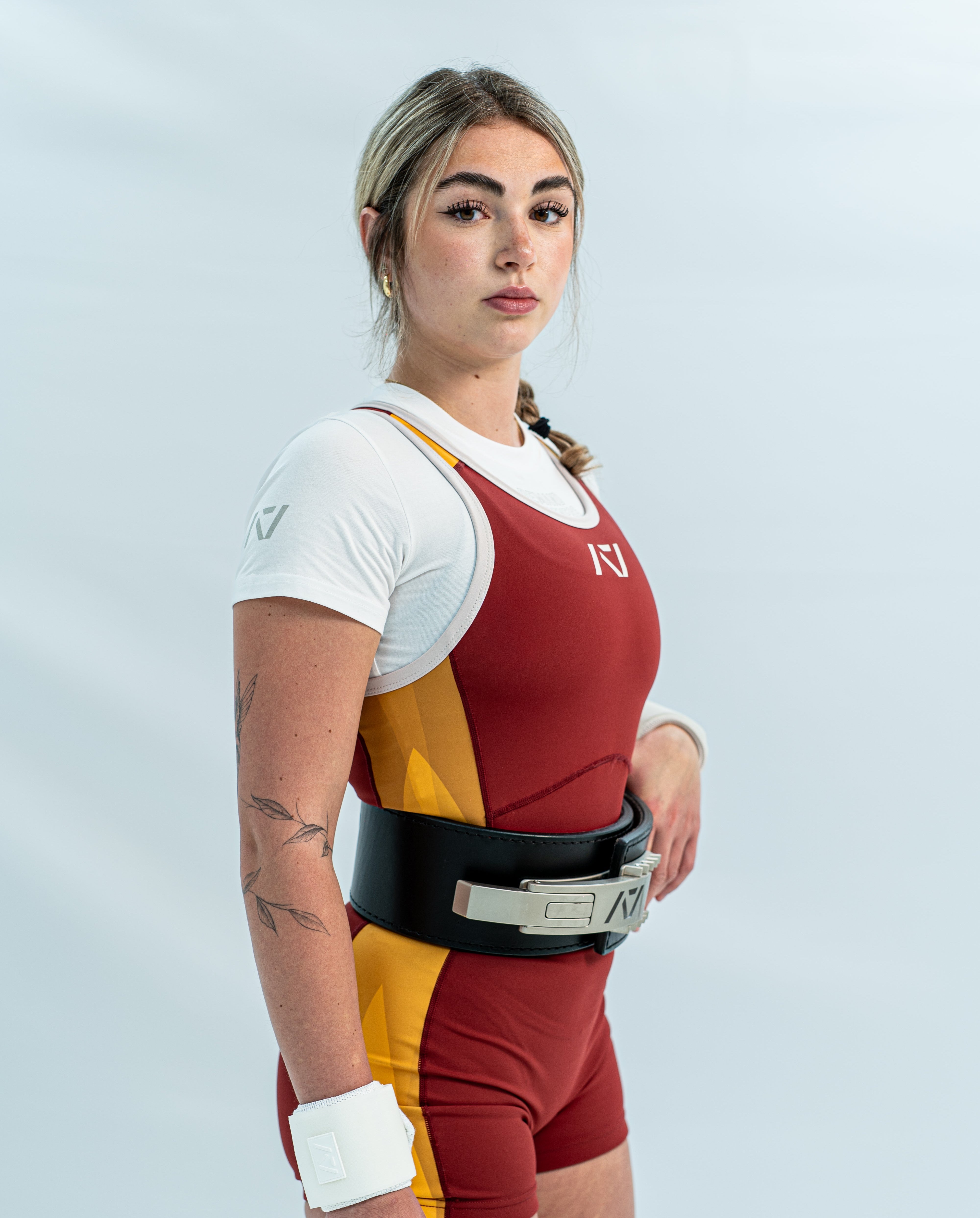 Female wearing a red and yellow rausch singlet with white accents on light gray background.