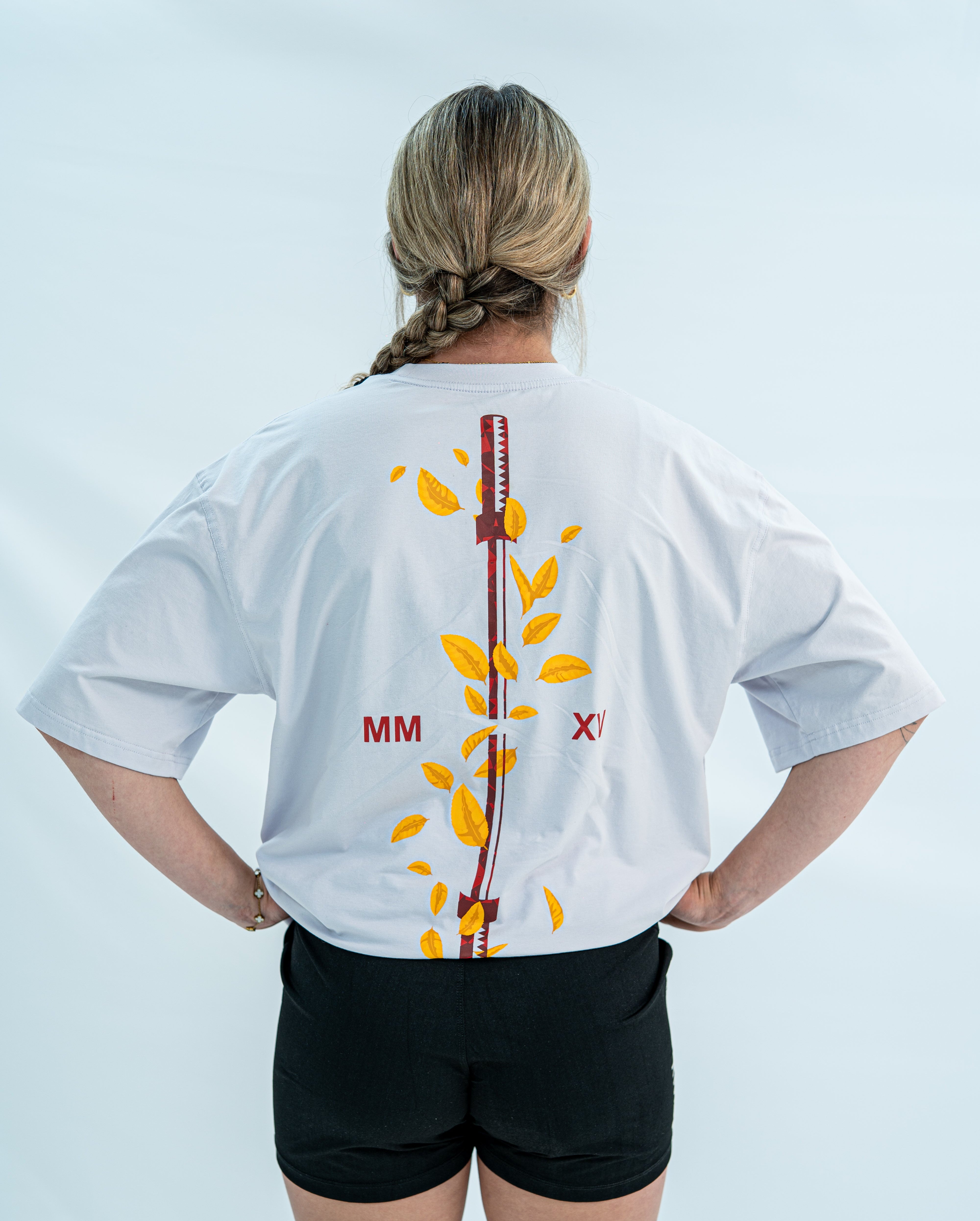 Female wearing a white over-fit shirt with a design on the back against a light gray background