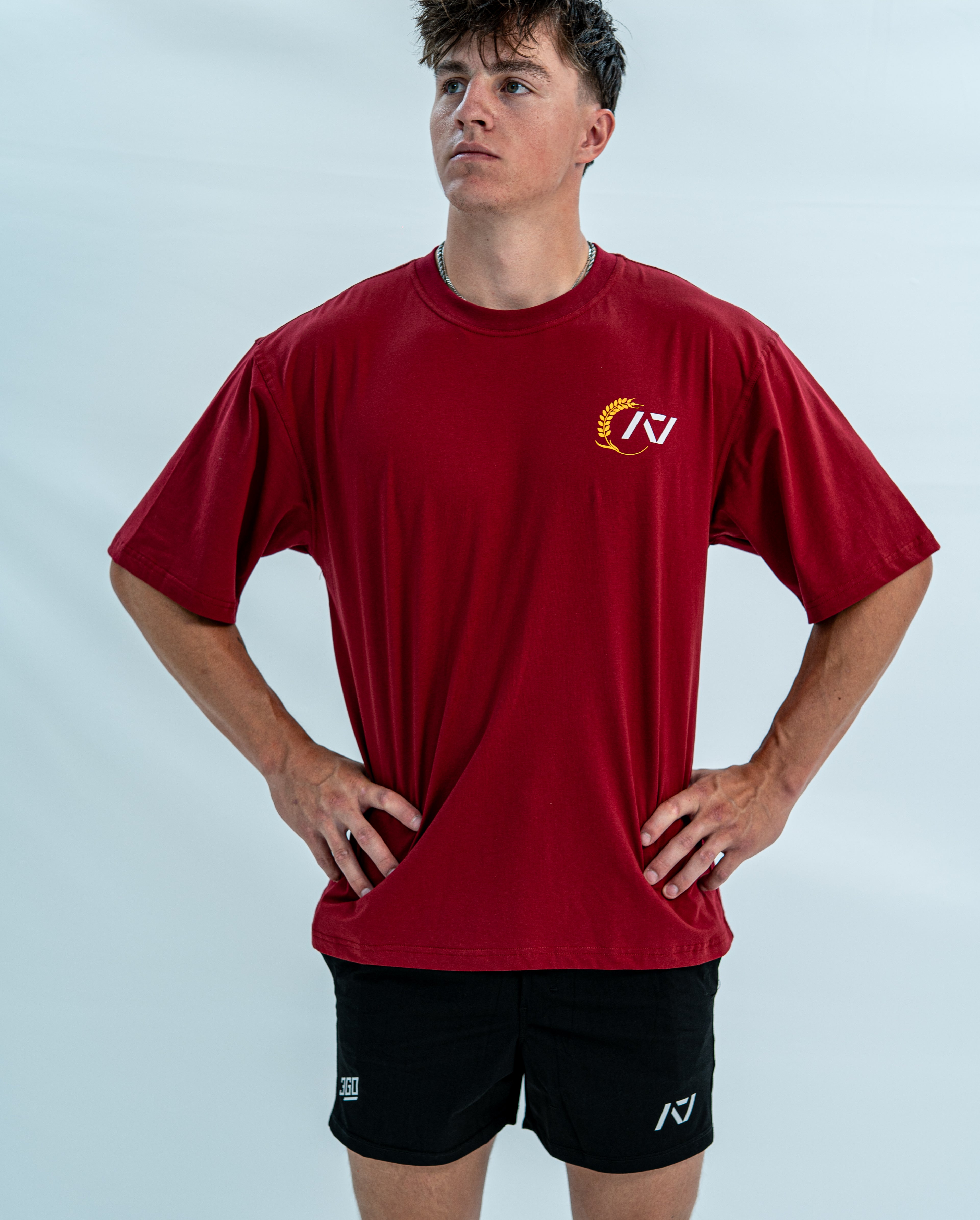 Male wearing a red over-fit unisex shirt with a logo on a light gray background