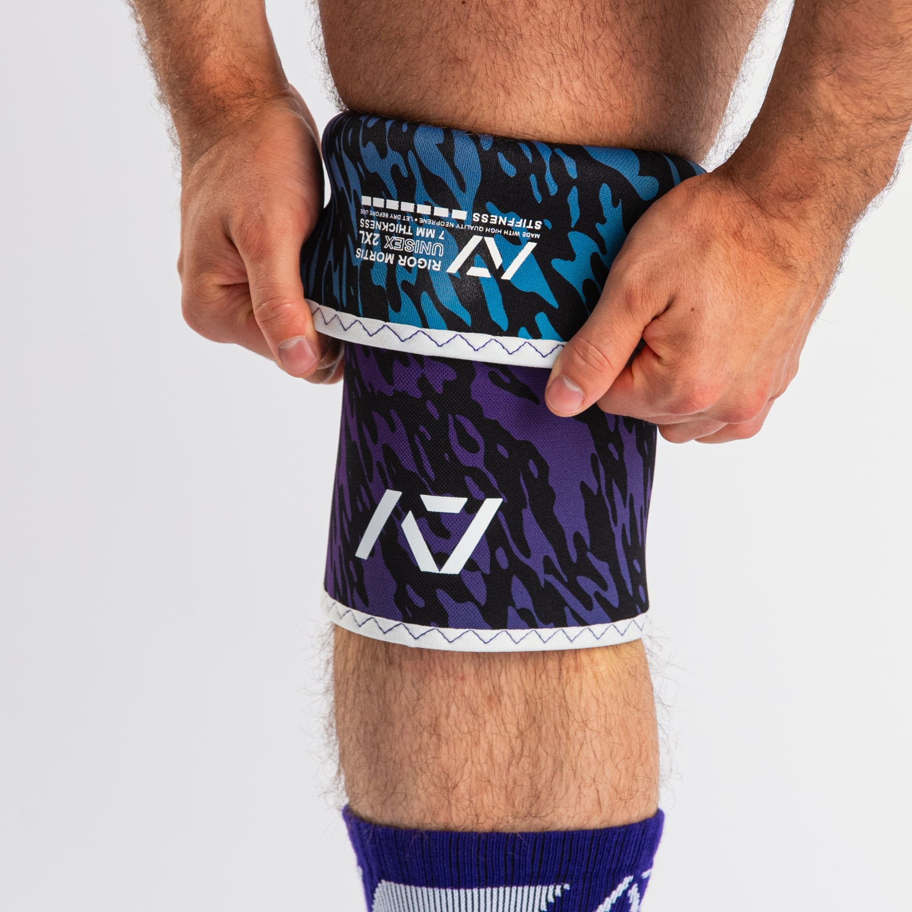 Front view of A7 Hourglass Knee Sleeves – Rigor Mortis – Violet Tiger on lifter's knees, highlighting label and the lifter putting the sleeve on.