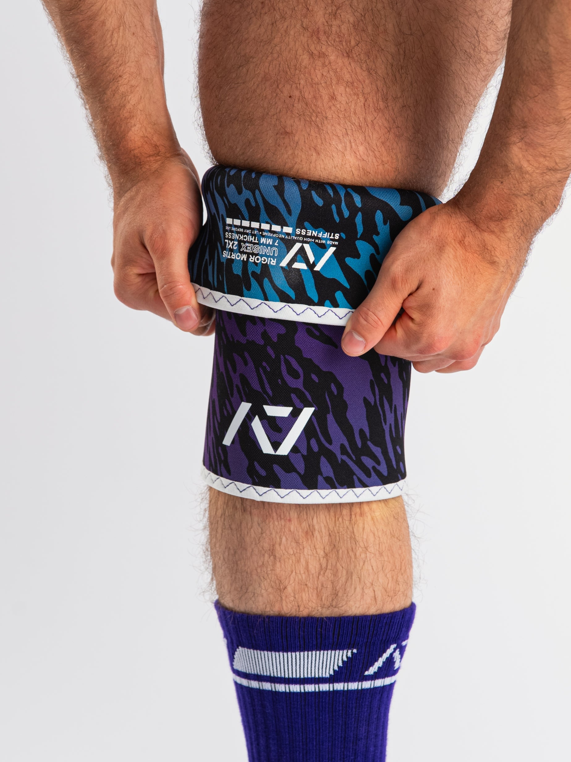 Front view of A7 Hourglass Knee Sleeves – Rigor Mortis – Violet Tiger on lifter's knees, highlighting label and the lifter putting the sleeve on.