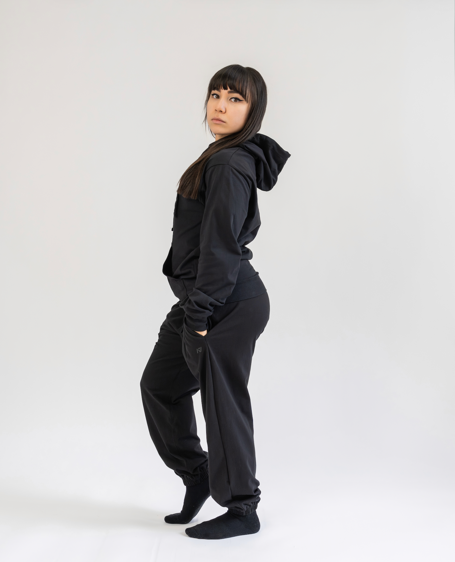 Person wearing a black hoodie and pants on a white background