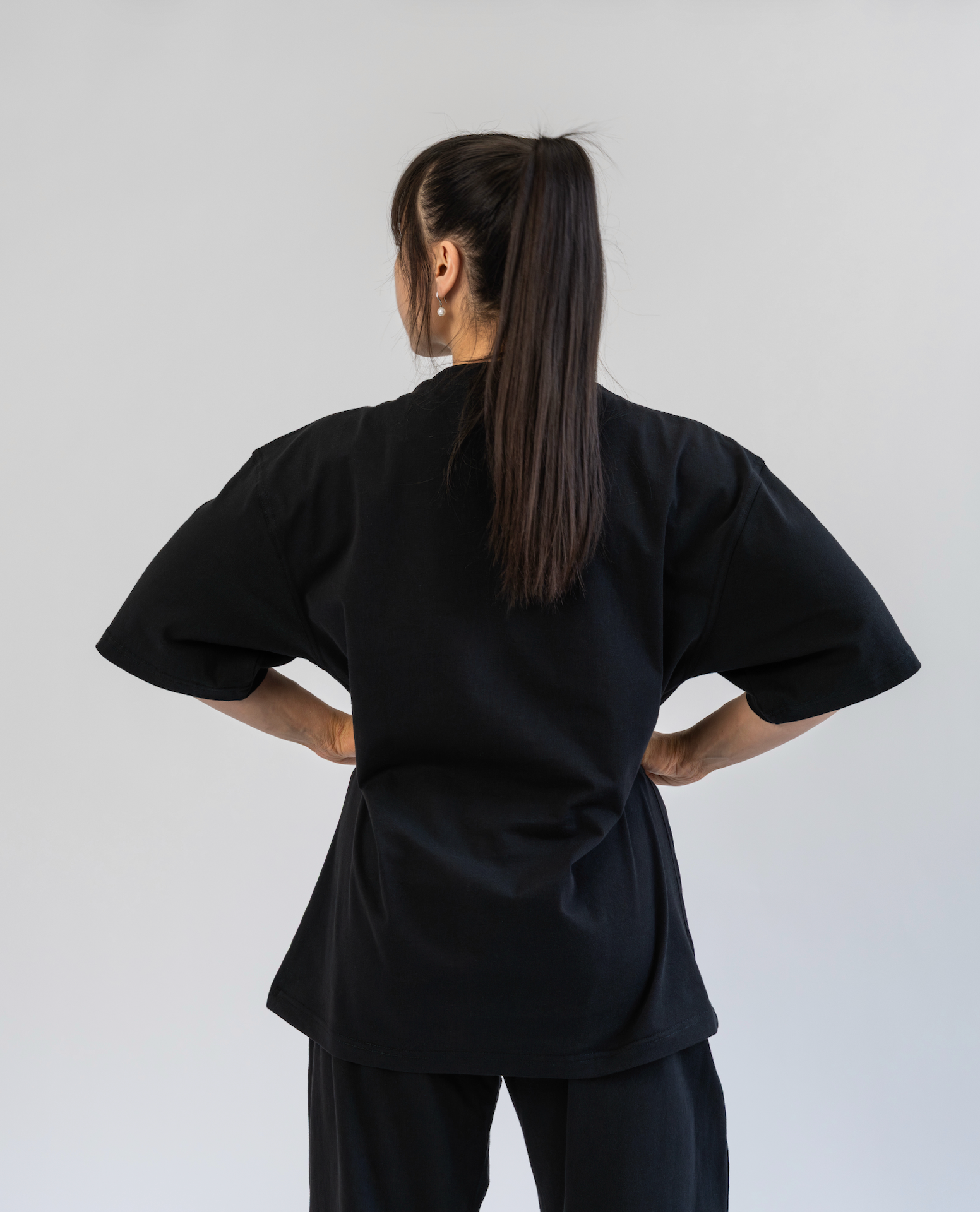 Person wearing a black outfit with wide sleeves and pants on a plain background