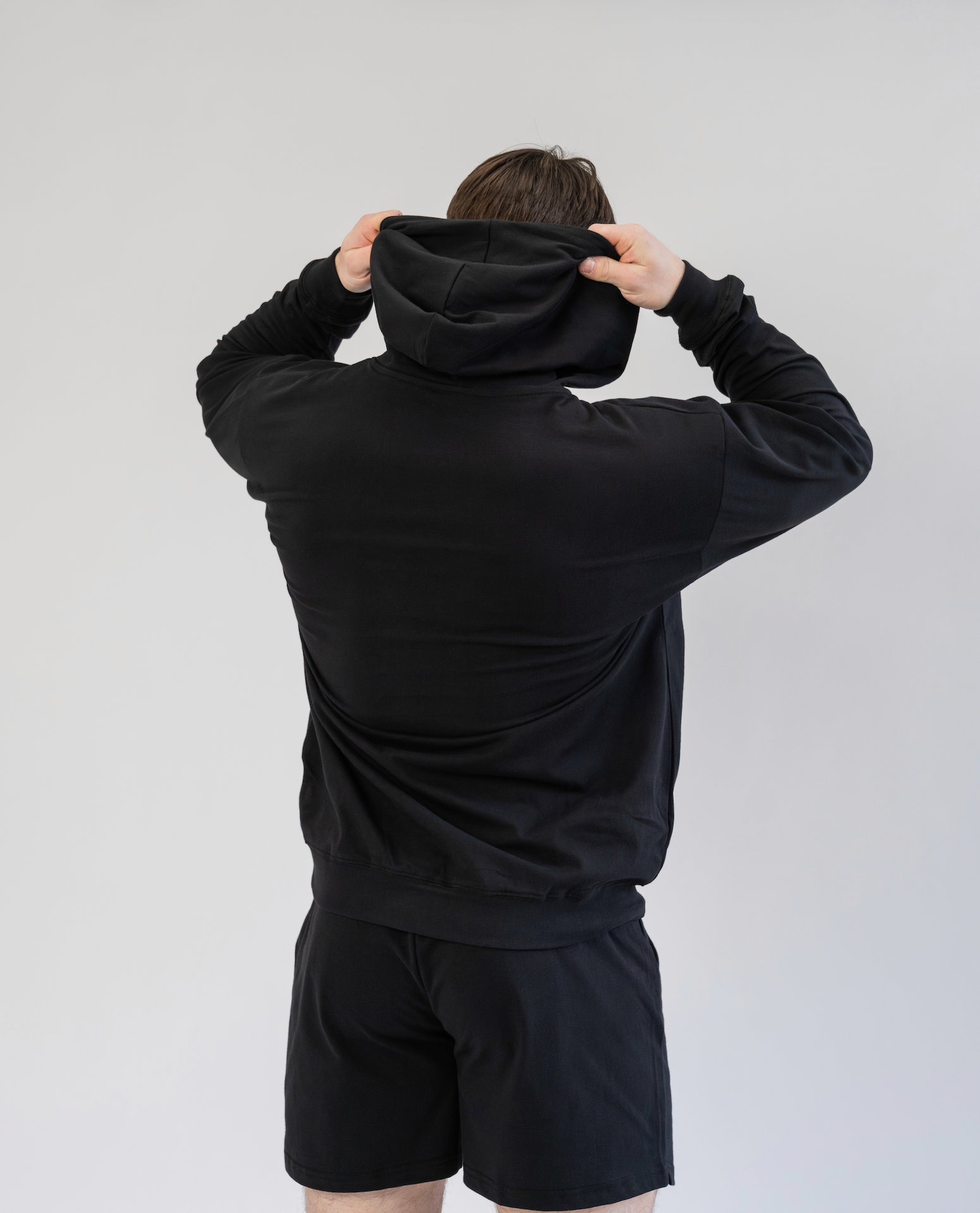 Person wearing a black hoodie and shorts set against a plain background