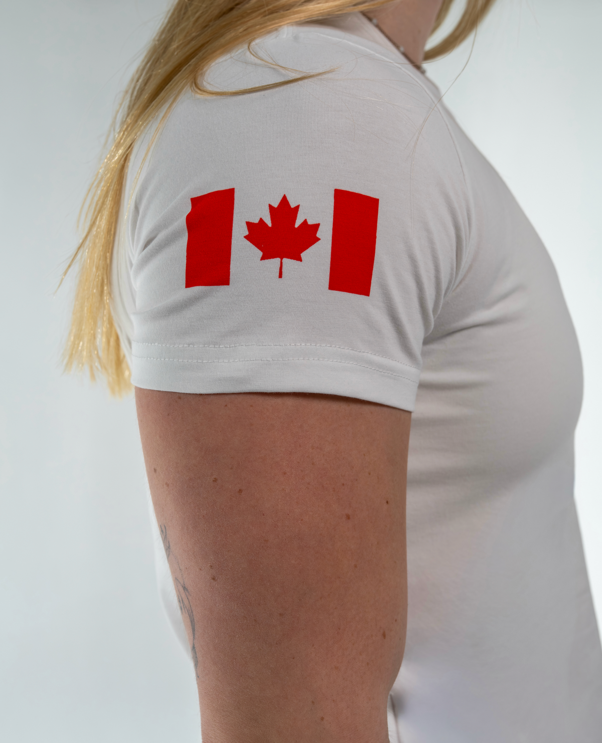 Person wearing a white t-shirt with a red maple leaf design on a plain background