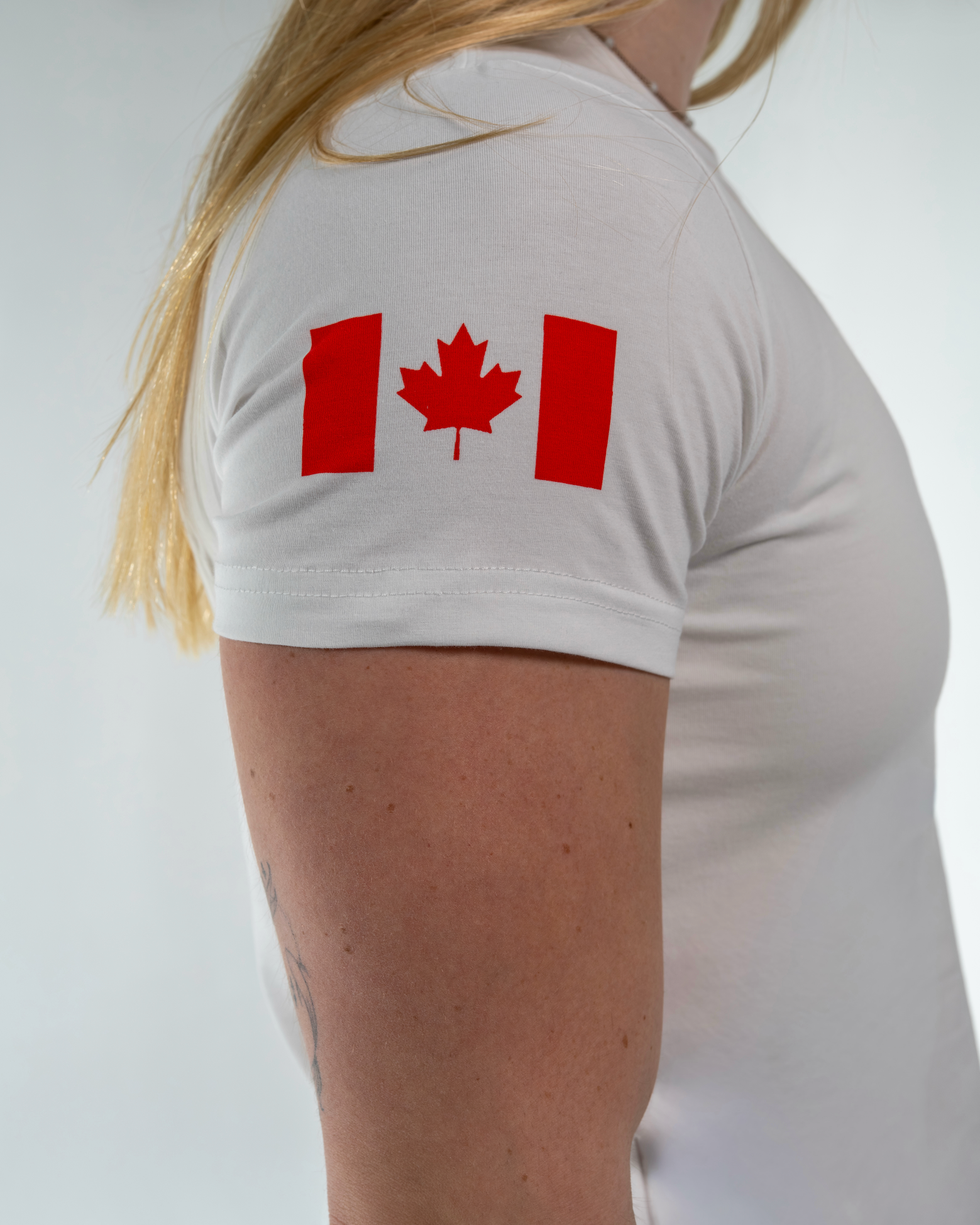 Person wearing a white t-shirt with a red maple leaf design on a plain background