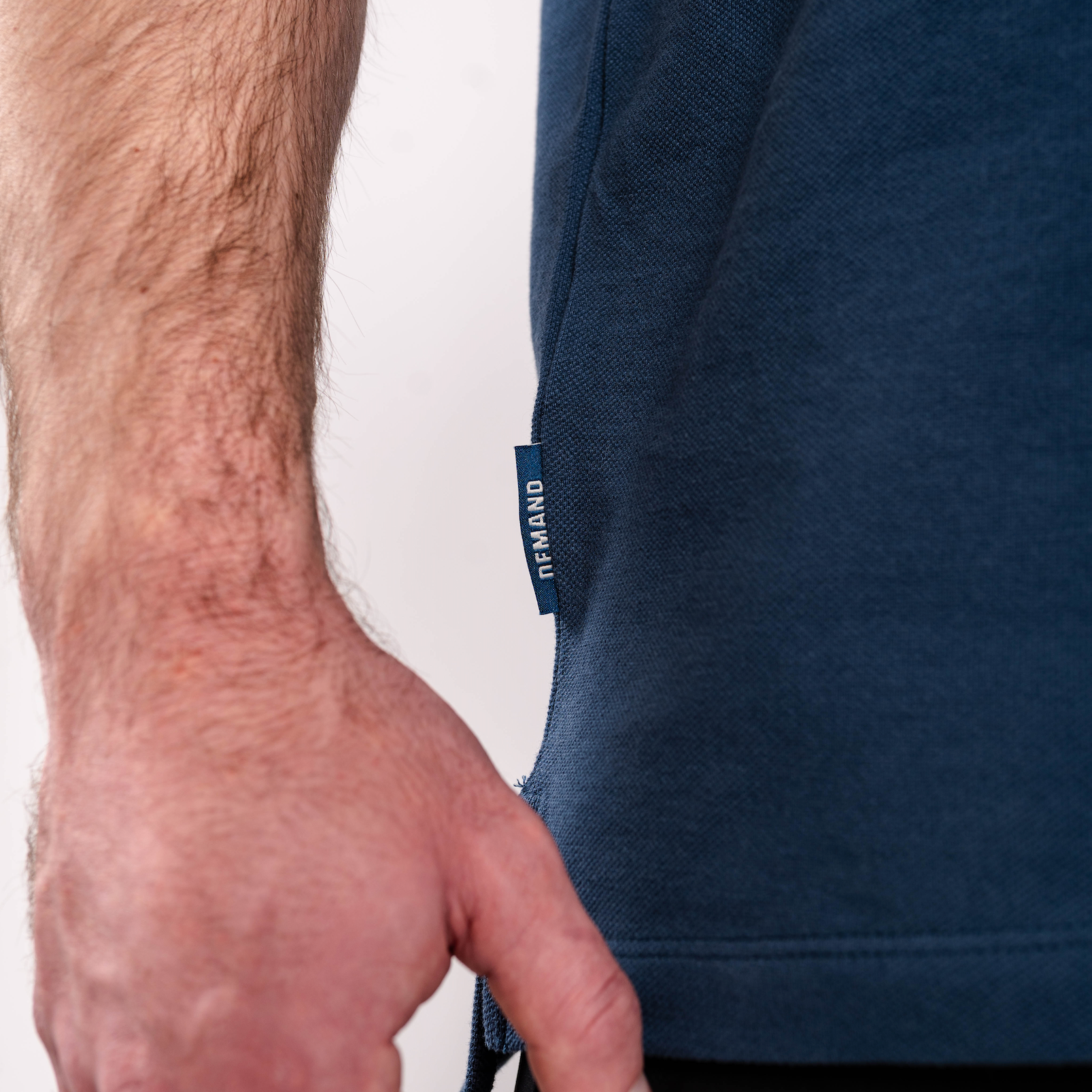 Close-up of the woven A7 hem tag on the Cotton Polo – Tides, stitched at the bottom hem for a subtle branded detail.