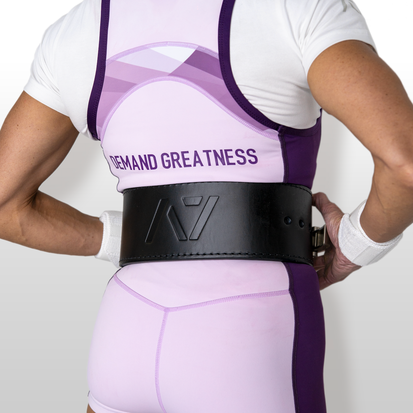 Person wearing a white and purple IPF approved powerlifting singlet with a black belt on a plain background