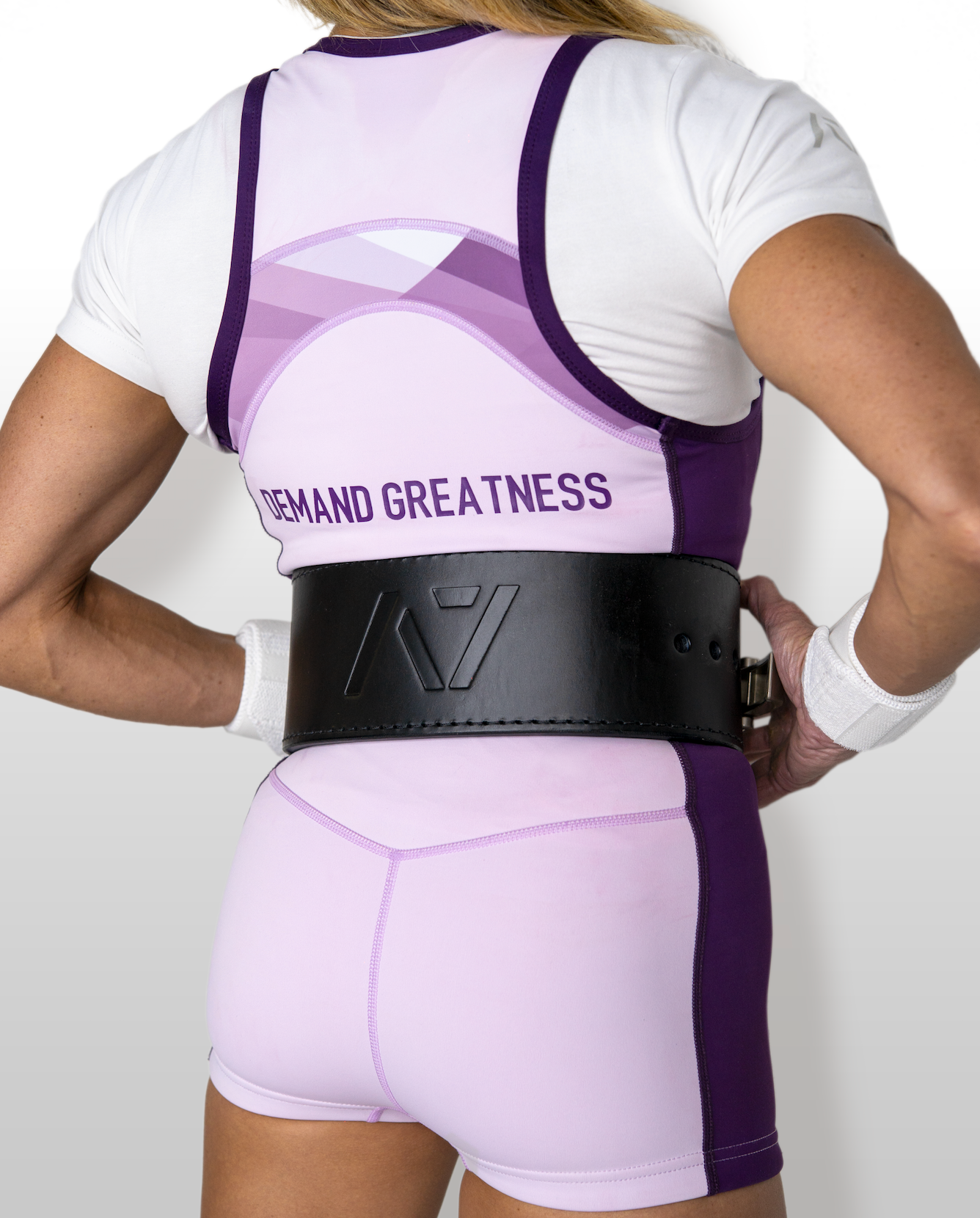 Person wearing a white and purple IPF approved powerlifting singlet with a black belt on a plain background