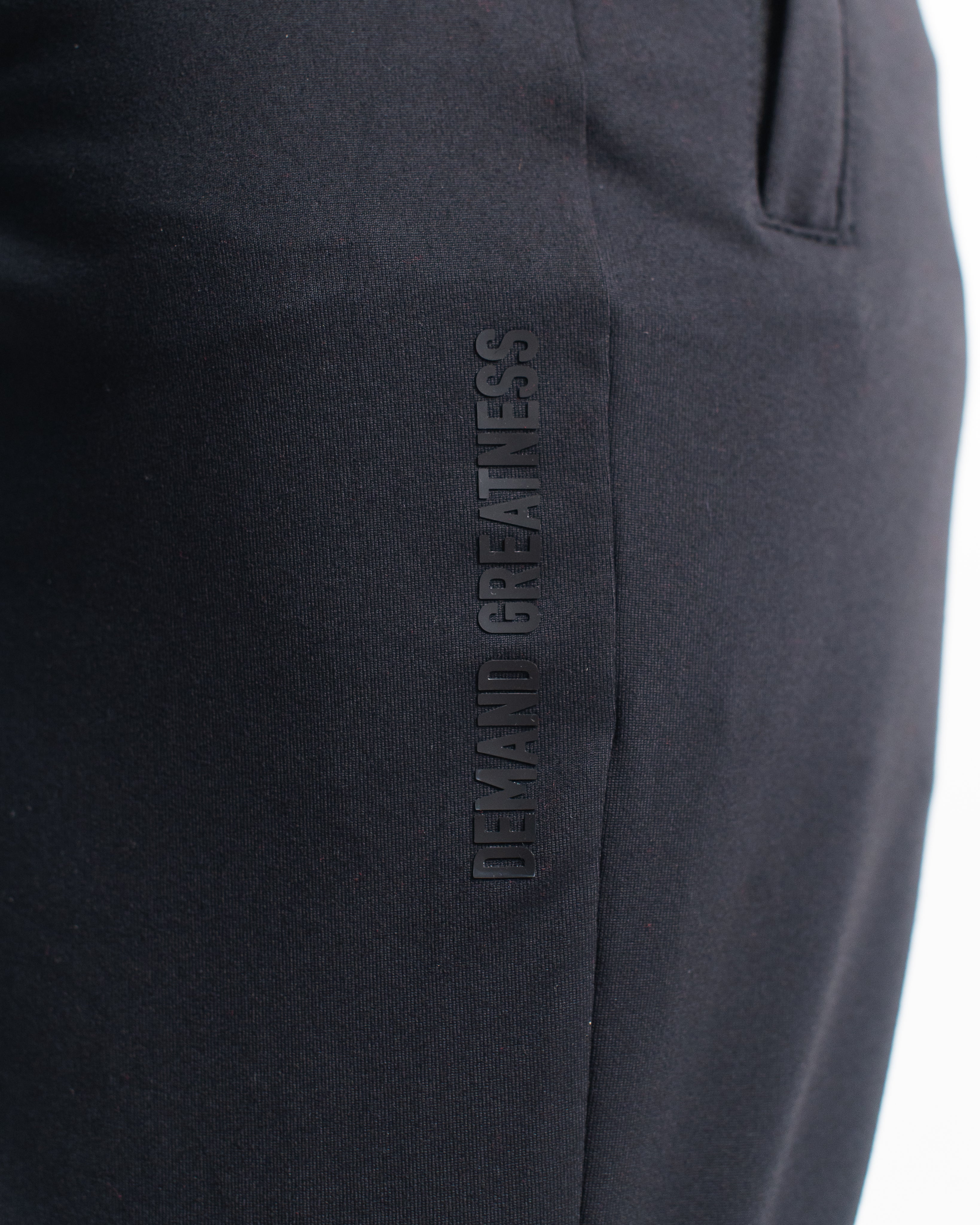 Close-up of “Demand Greatness” text printed vertically on the quad of the Stealth Defy Joggers, showcasing subtle matte branding along the leg.