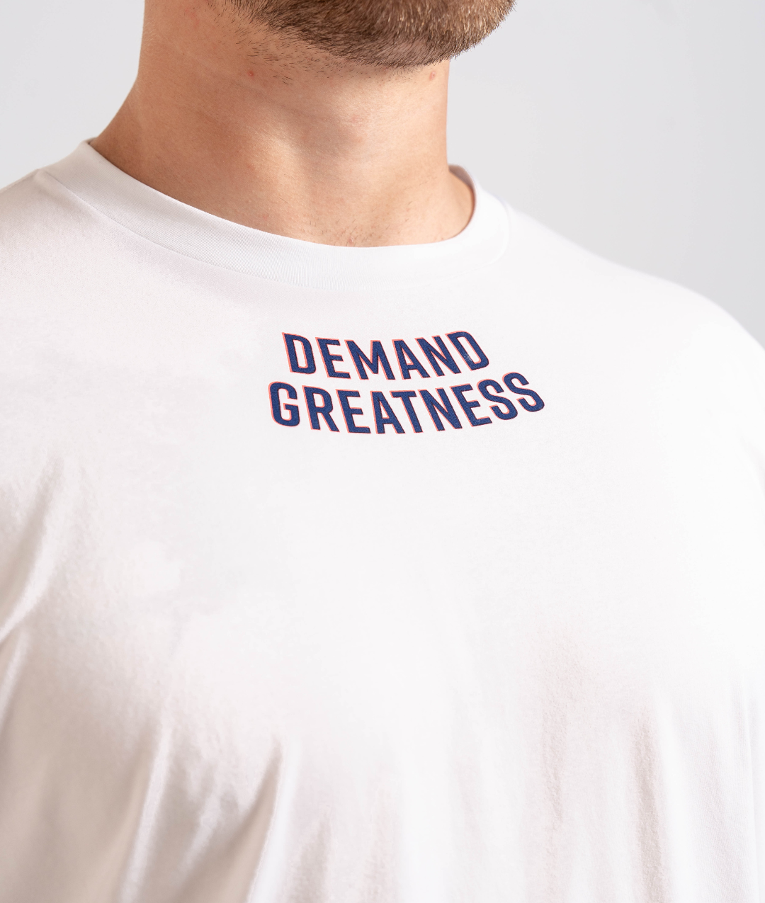 Close-up of the “Demand Greatness” print across the chest of the Americana True-Fit Meet Shirt, featuring bold typography in red, white, and blue.