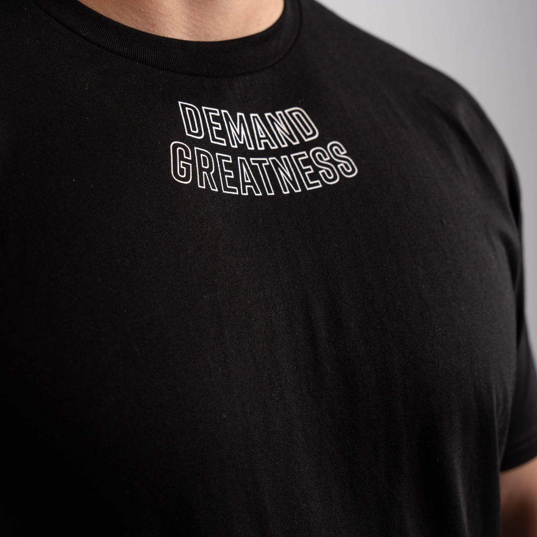 Close-up of “Demand Greatness” print across the chest of the Domino True‑Fit Men’s Meet Shirt, highlighting bold monochrome lettering on soft stretch fabric.