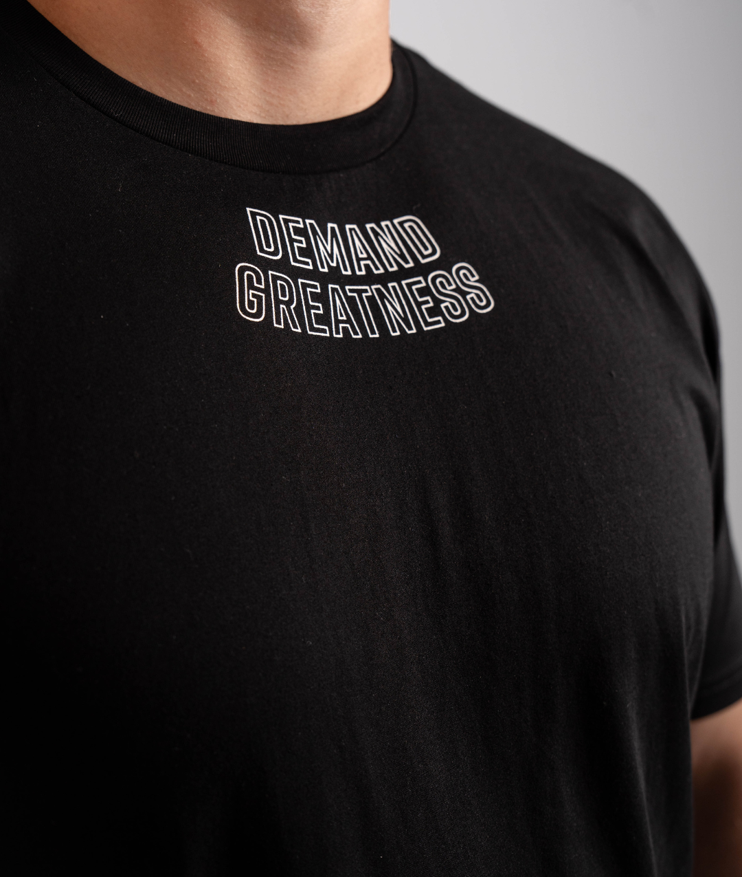Close-up of “Demand Greatness” print across the chest of the Domino True‑Fit Men’s Meet Shirt, highlighting bold monochrome lettering on soft stretch fabric.