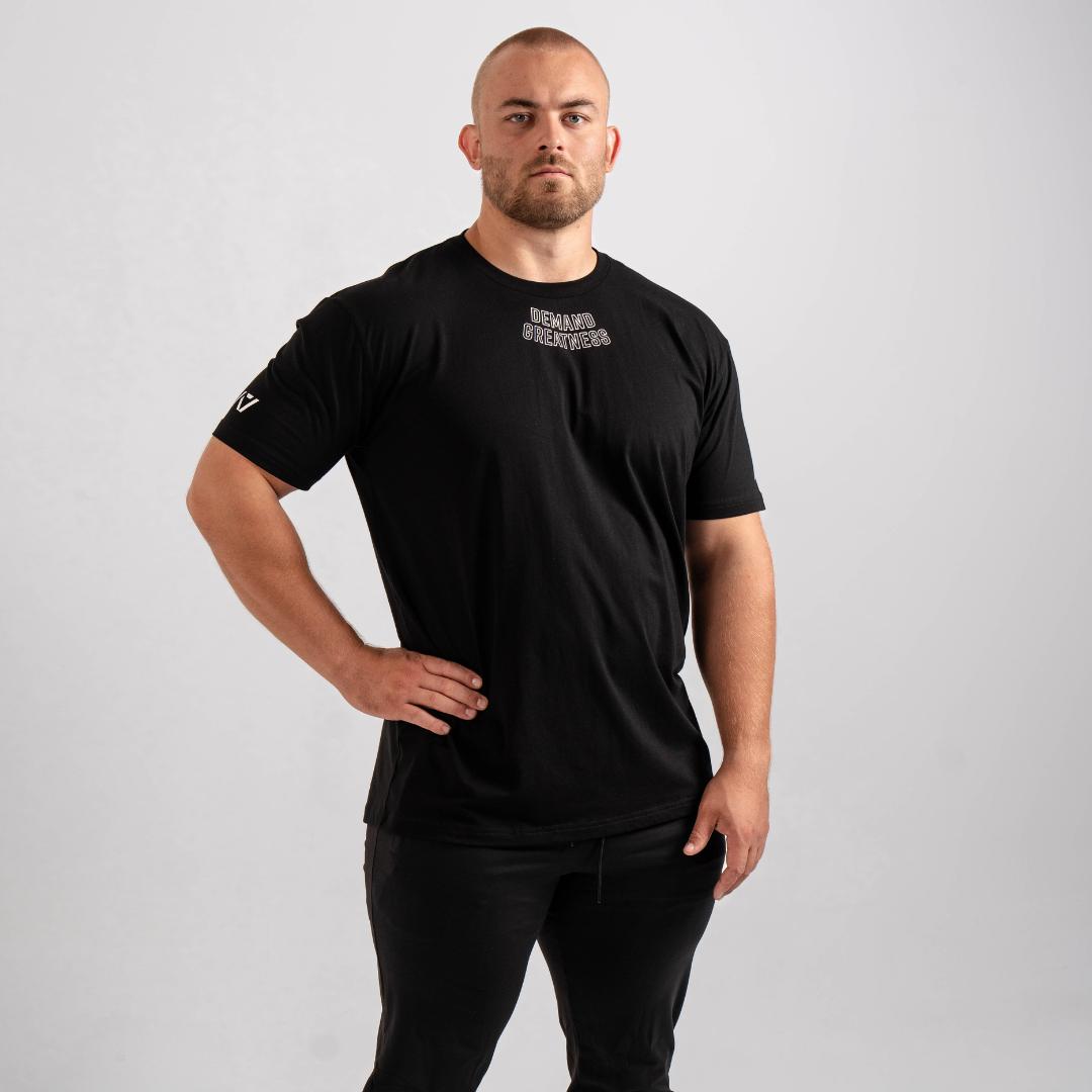 Front view of the Domino True‑Fit Meet Shirt showcasing the “Demand Greatness” print and athletic torso fit.