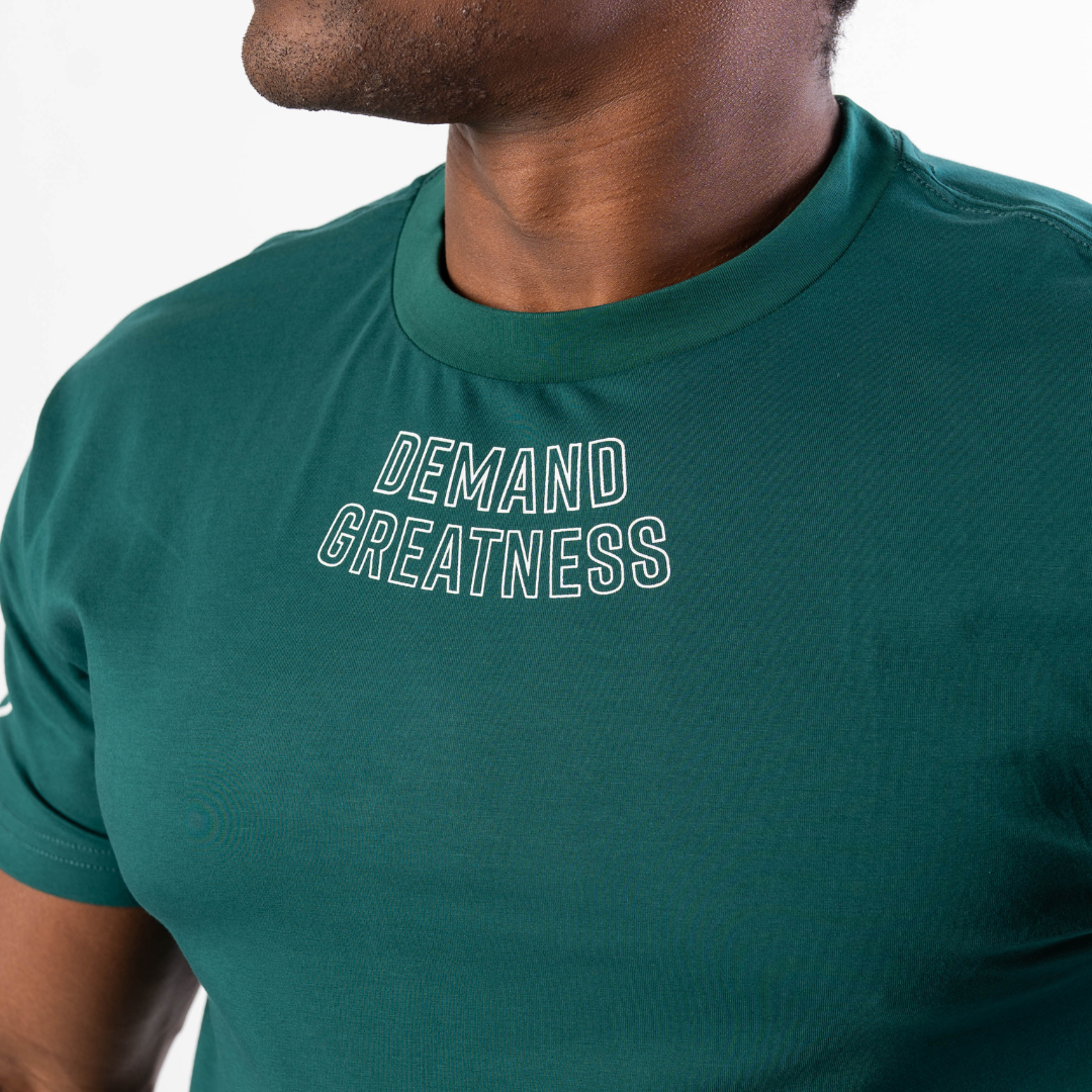 Close-up of “Demand Greatness” chest print on the Emerald Forás True‑Fit Meet Shirt, with bold white typography contrasting against rich green stretch fabric.