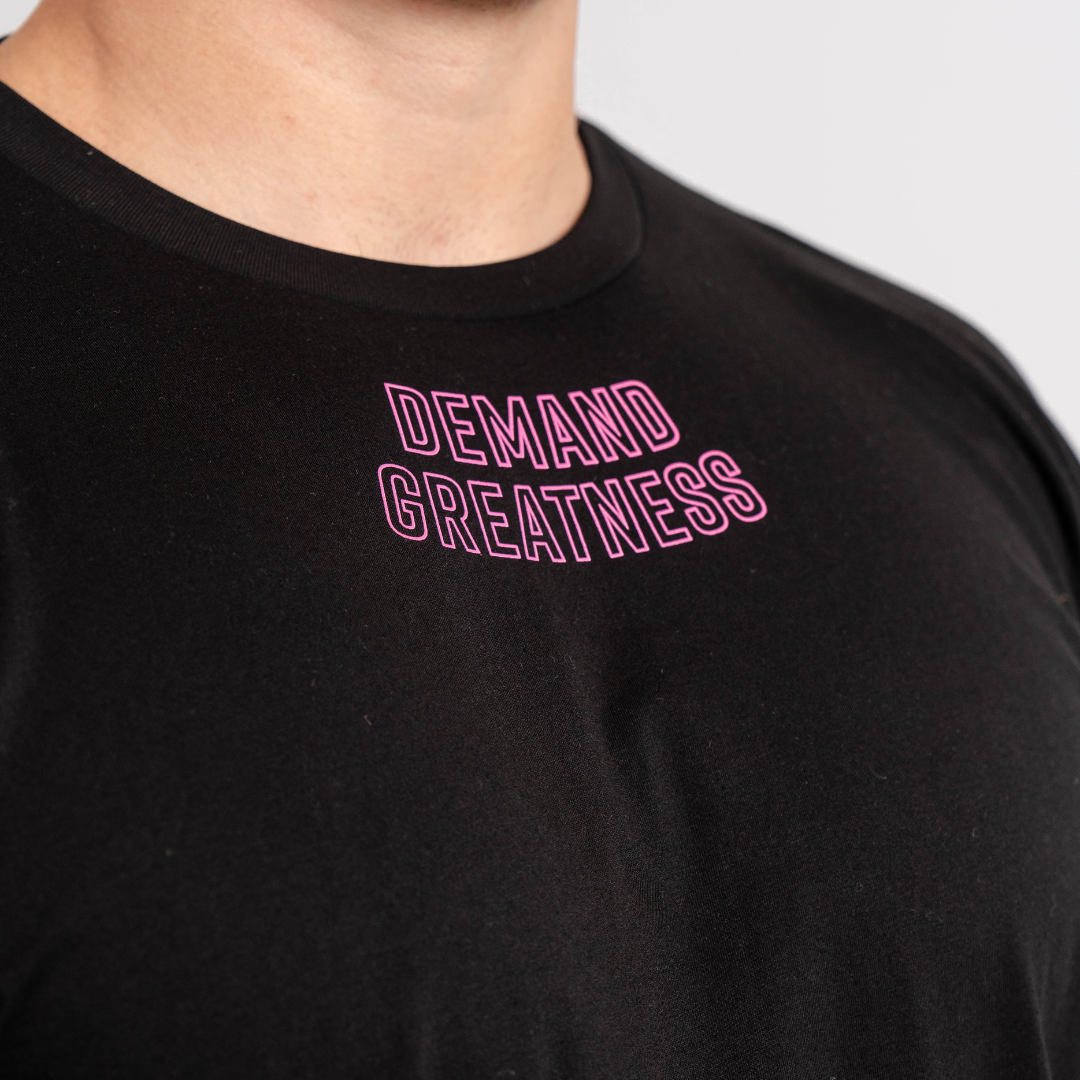 Close-up of “Demand Greatness” printed across the chest of the Flamingo True‑Fit Meet Shirt, with bold white text standing out on vibrant pink fabric.