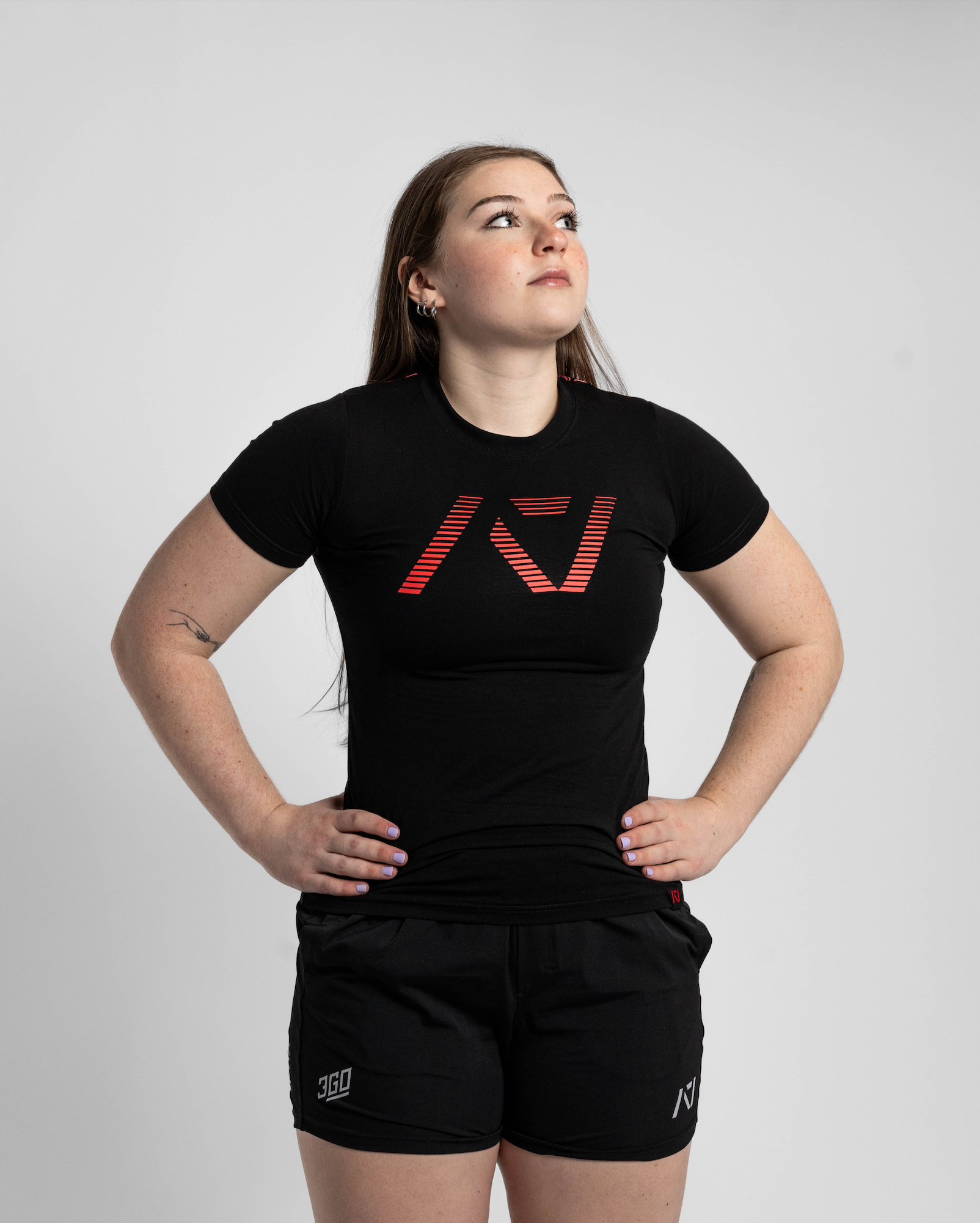 Person wearing a black t-shirt with a logo and black shorts on a light gray background