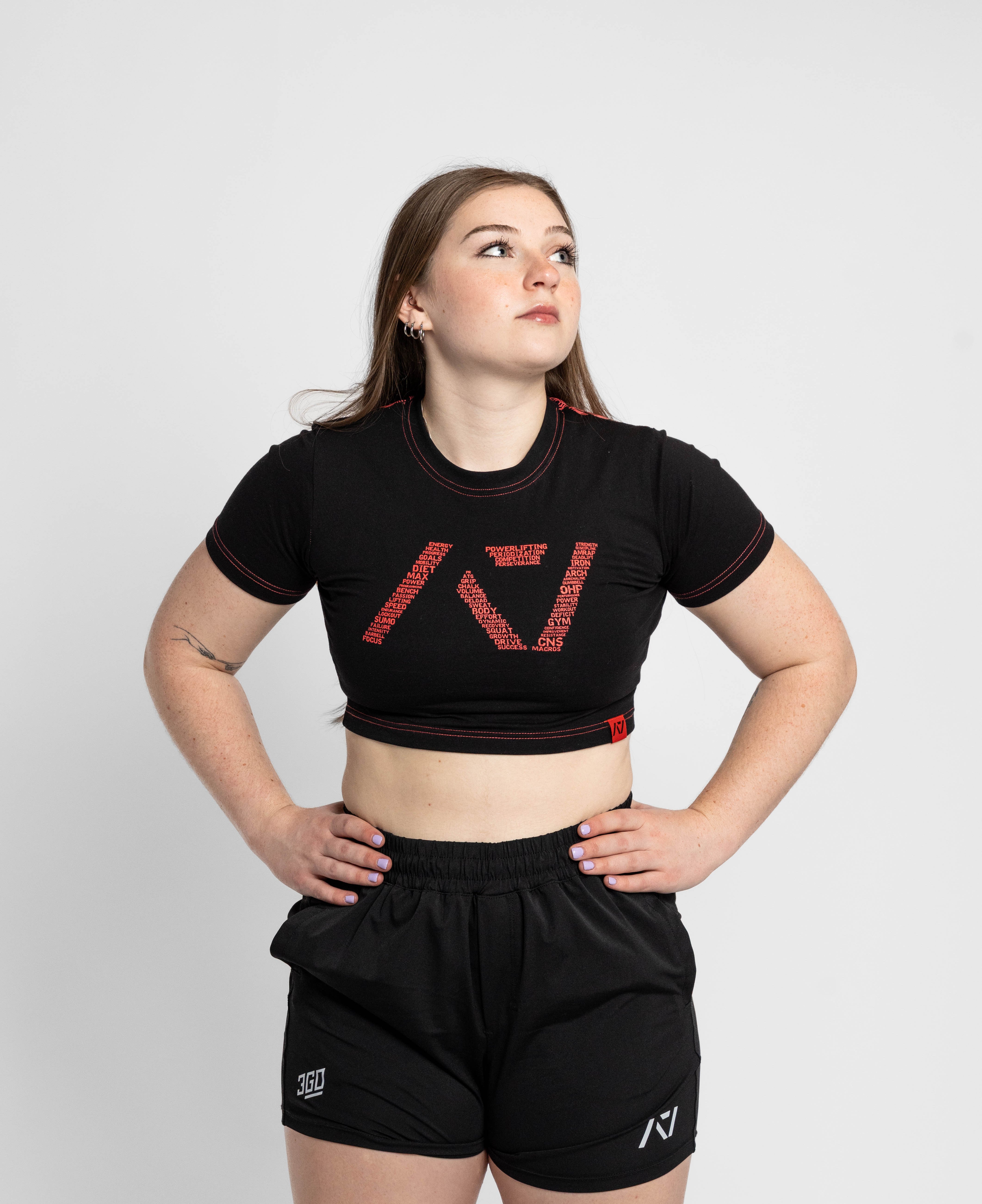 Woman wearing a black crop top and shorts with a brand logo on a white background
