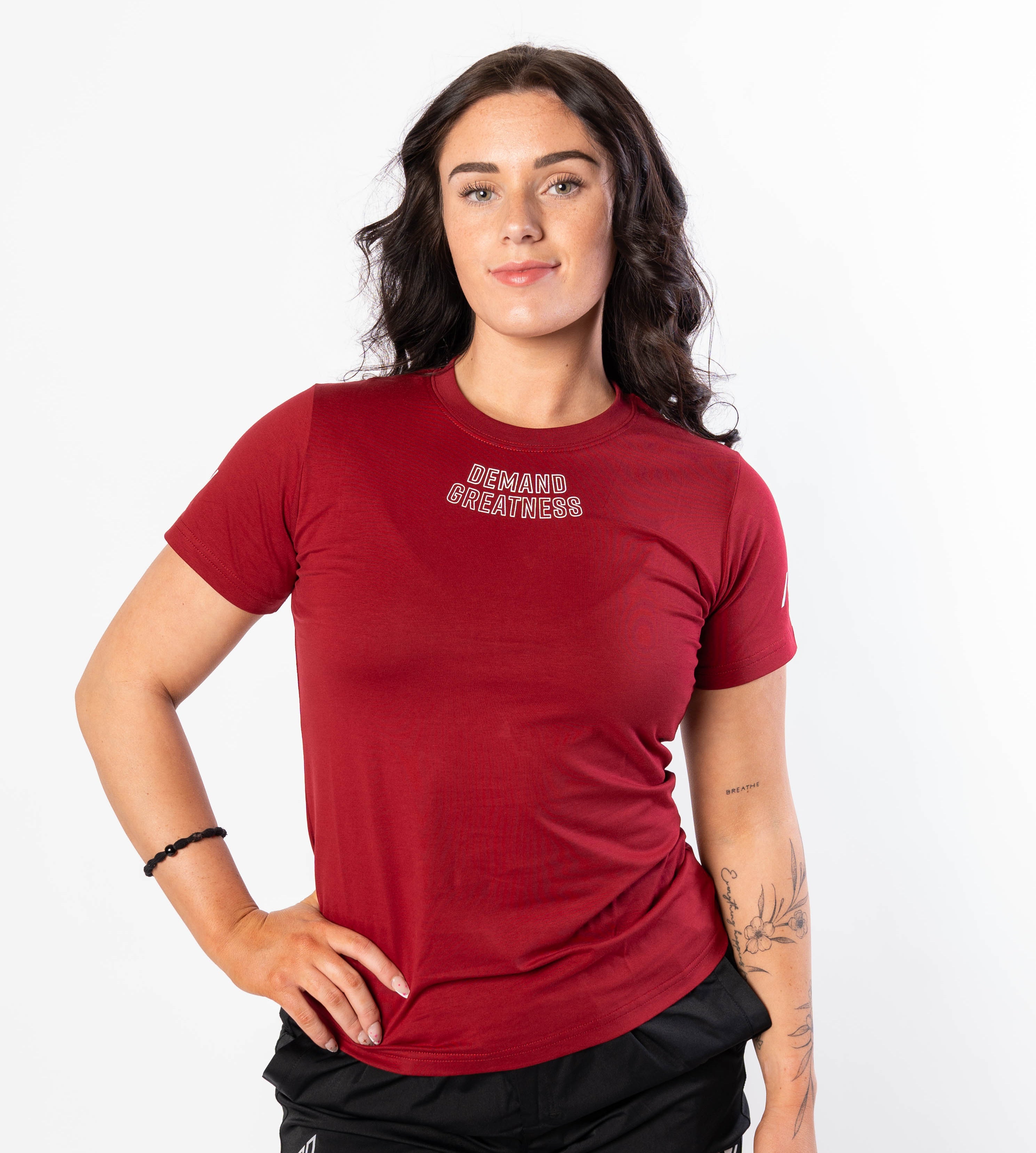 A woman wearing a red Demand Greatness True-Fit women's meet shirt with a logo on the upper chest and upper back.