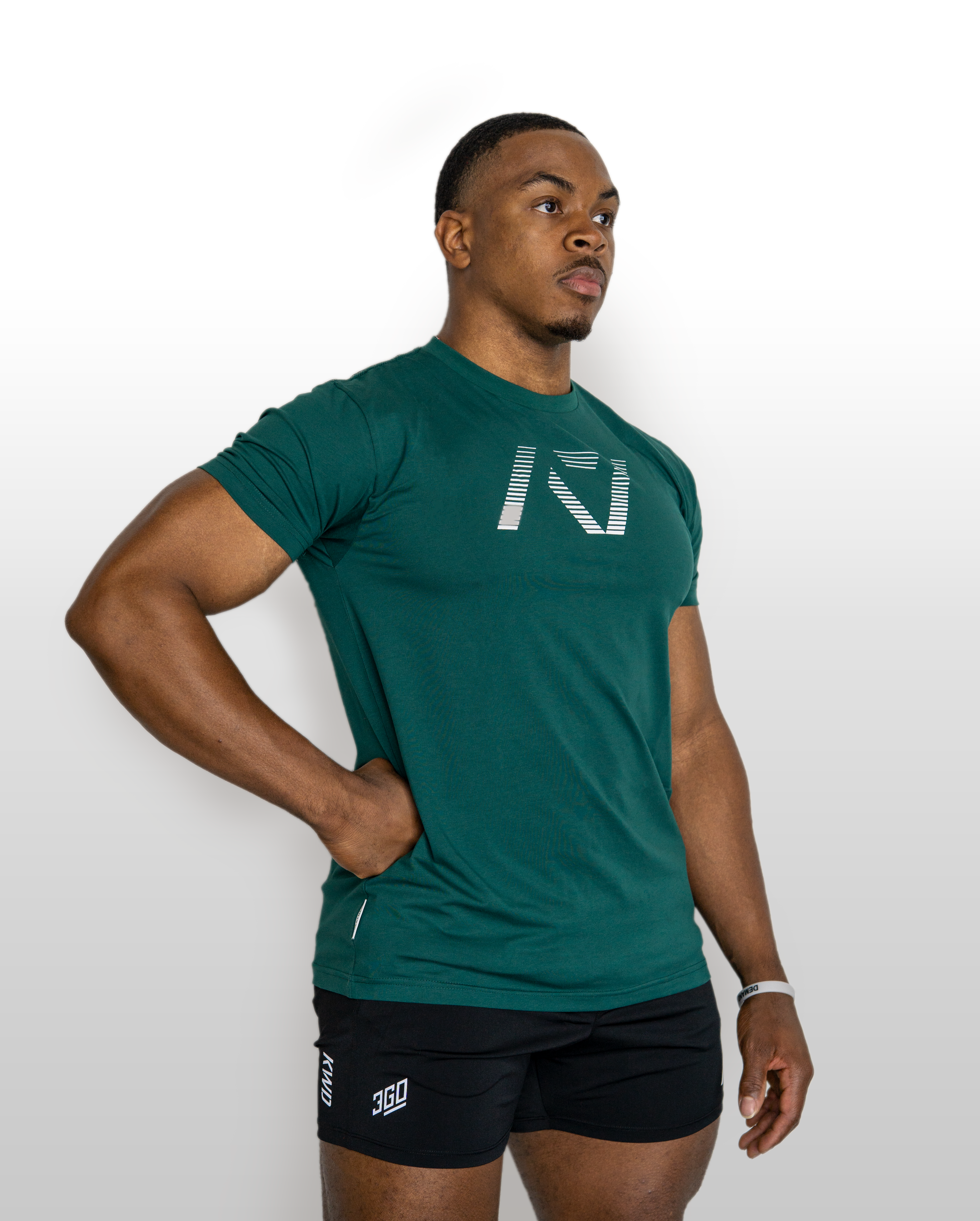 Man wearing a green athletic shirt and black shorts with a logo on a white background