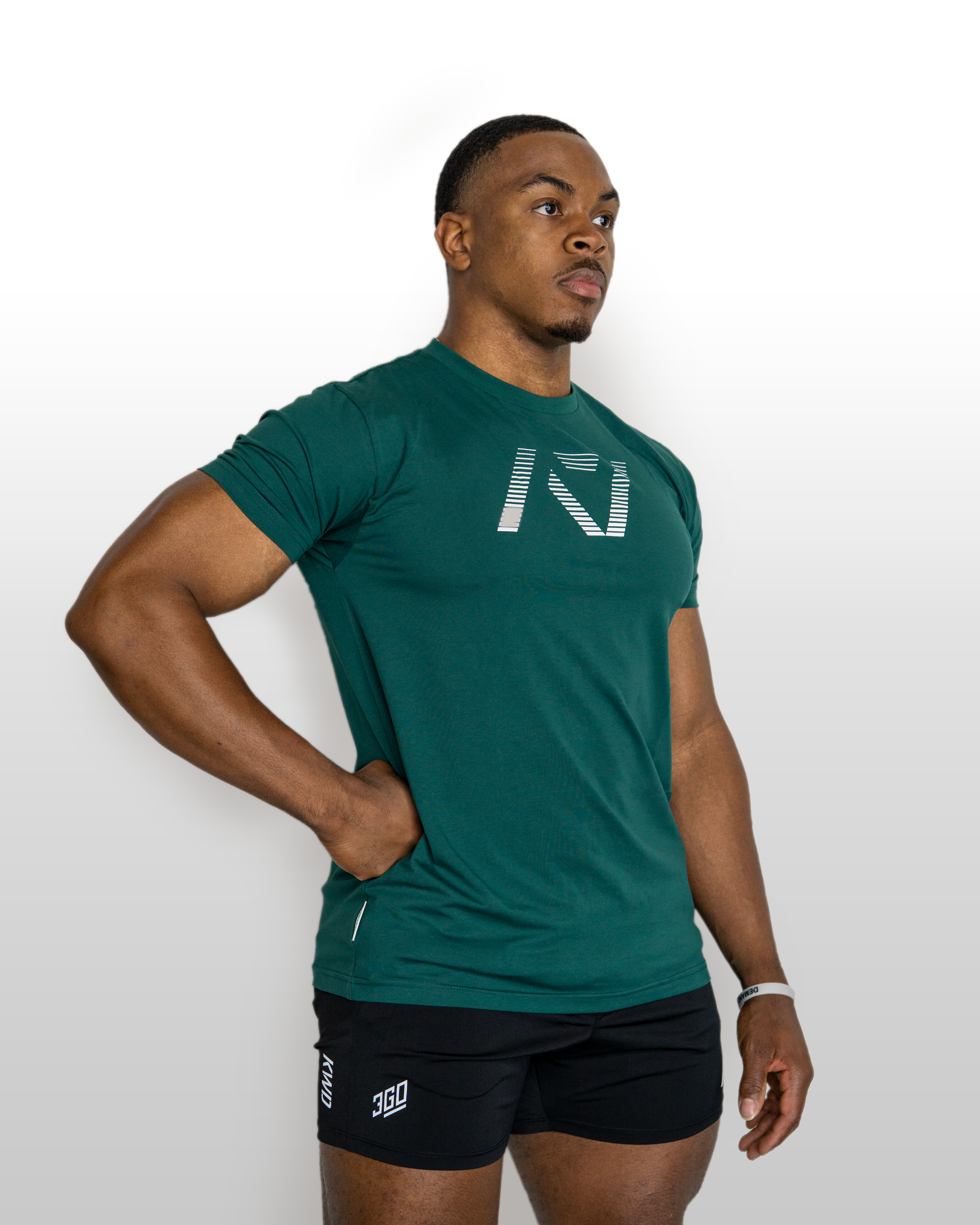 Man wearing a green athletic shirt and black shorts with a logo on a white background