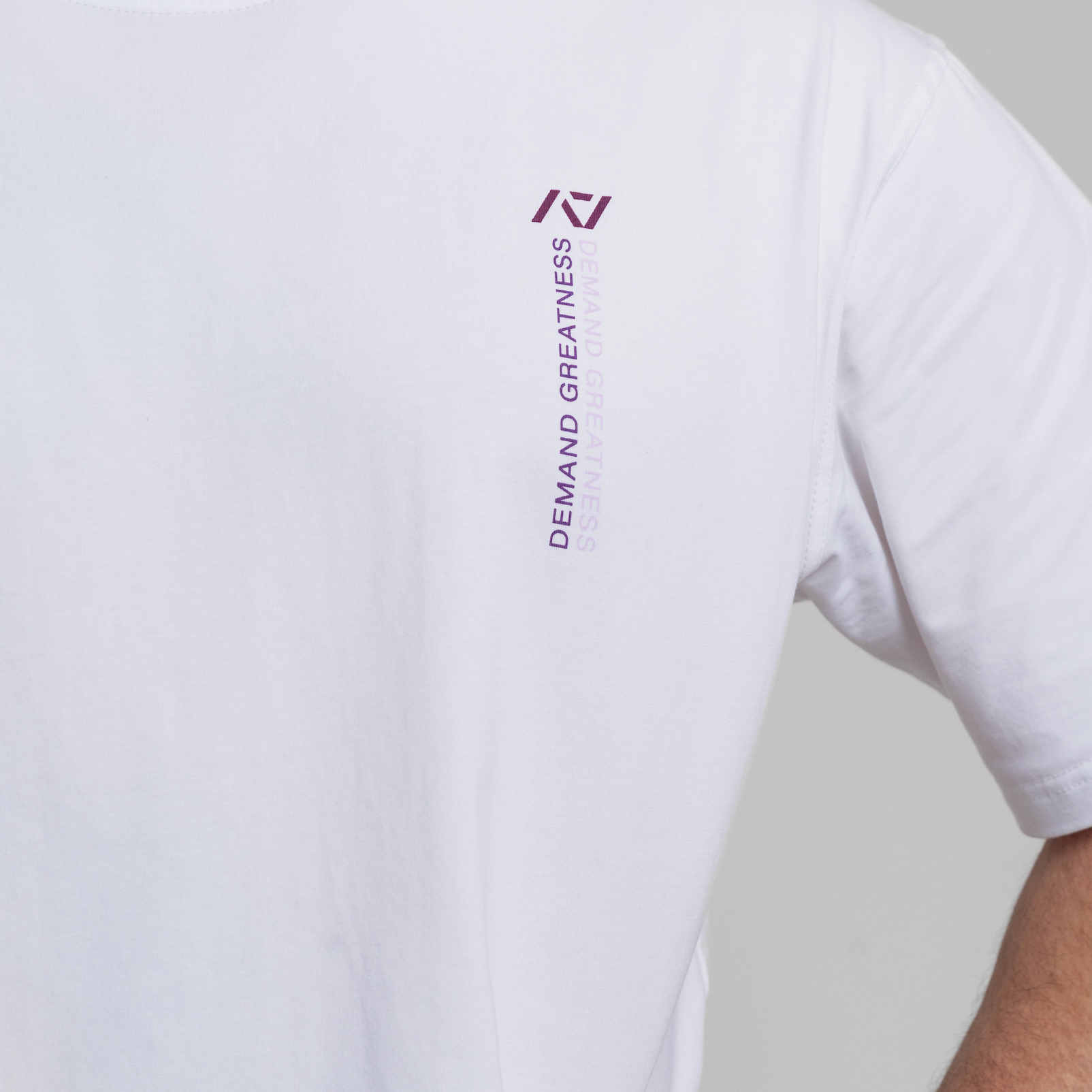 White t-shirt with a logo and text on the sleeve against a gray background