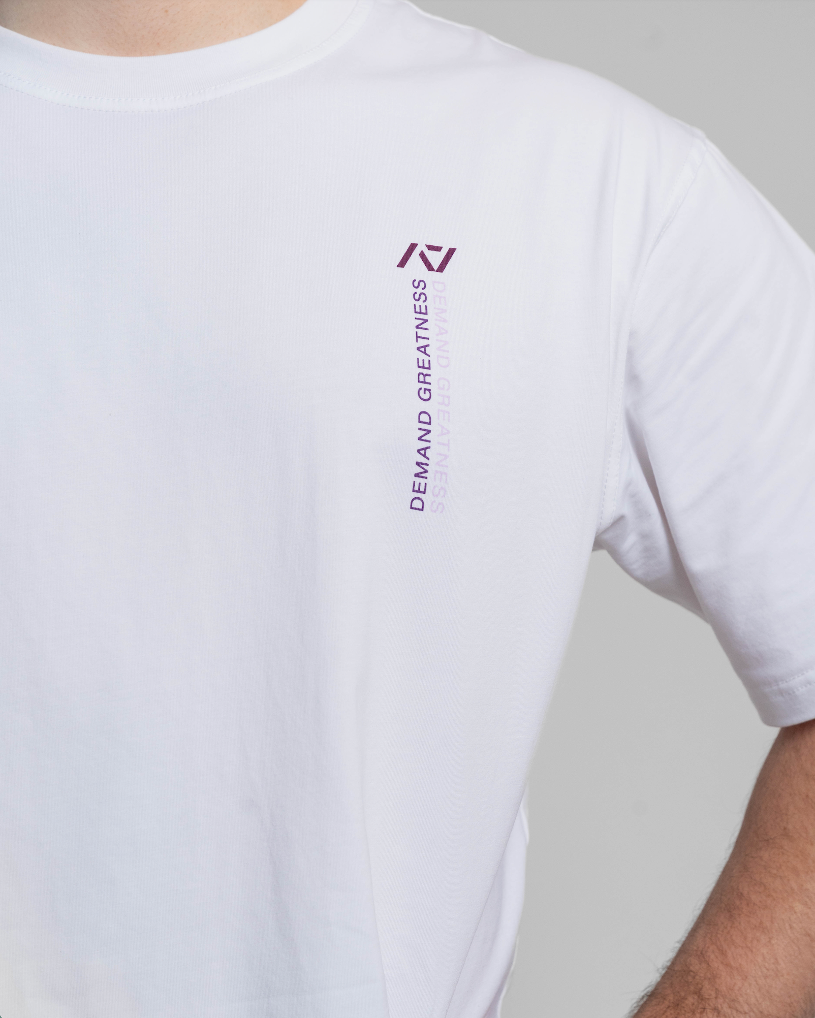 White t-shirt with a logo and text on the sleeve against a gray background