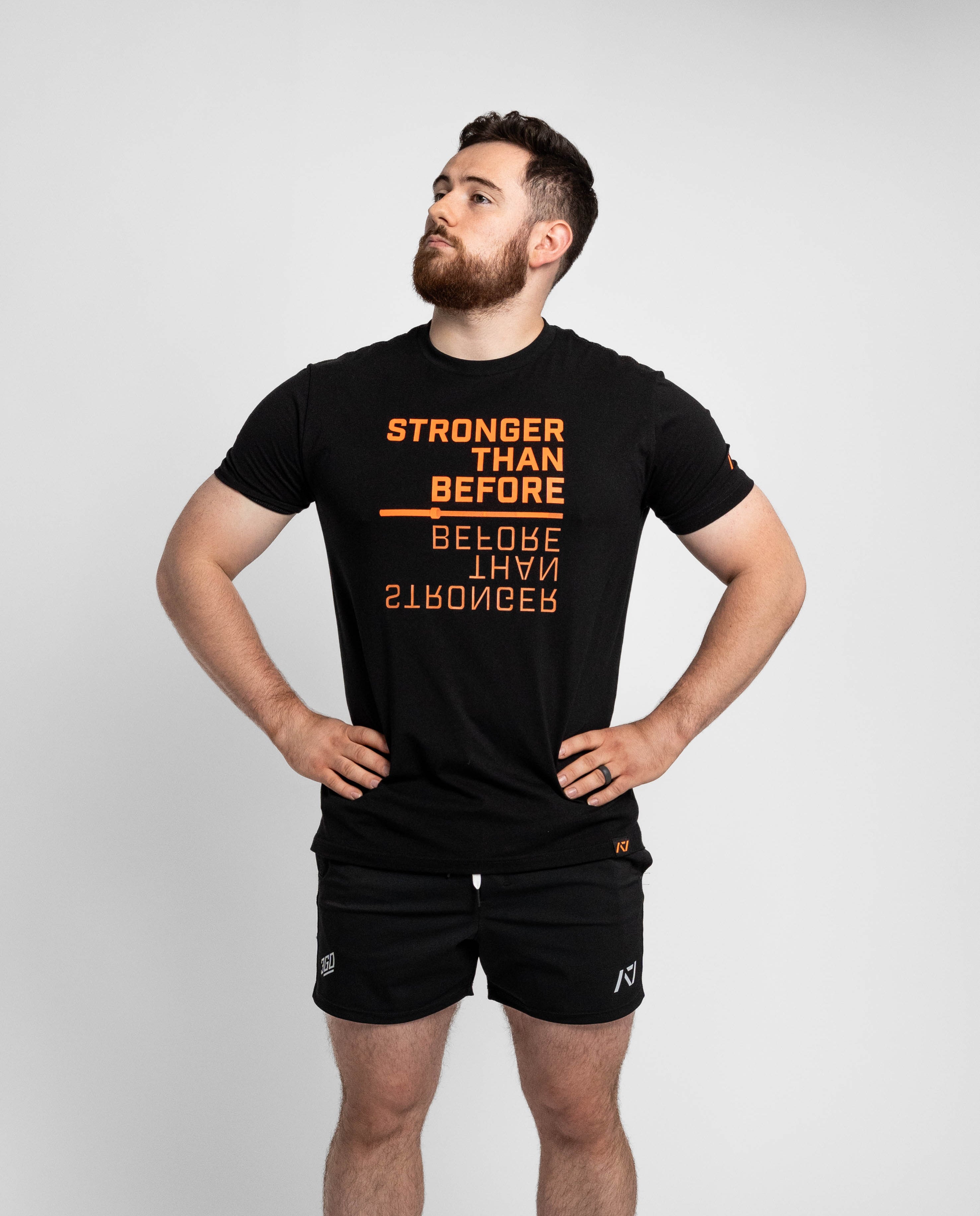 Man wearing a black t-shirt with orange text and black shorts on a light gray background