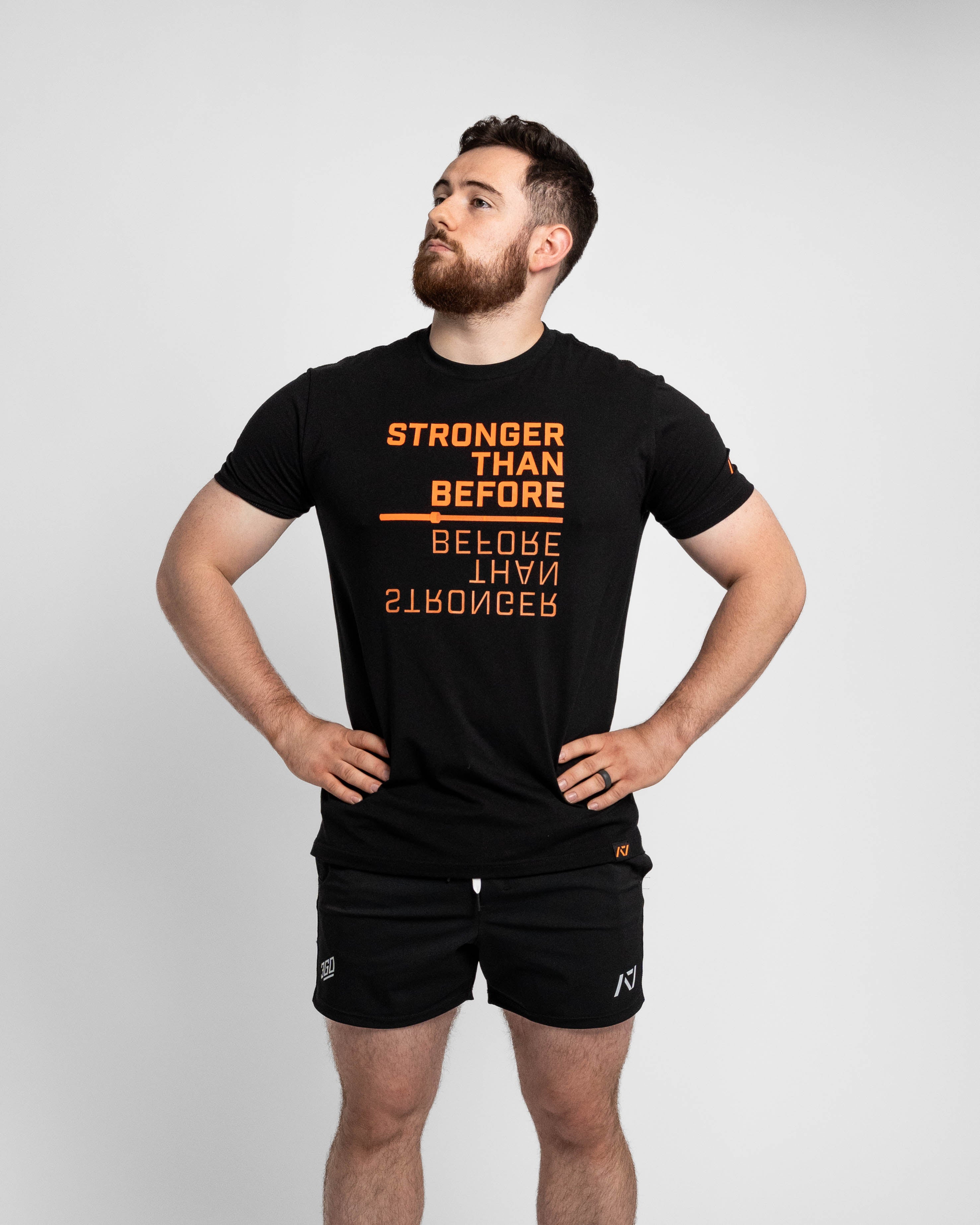 Man wearing a black t-shirt with orange text and black shorts on a light gray background