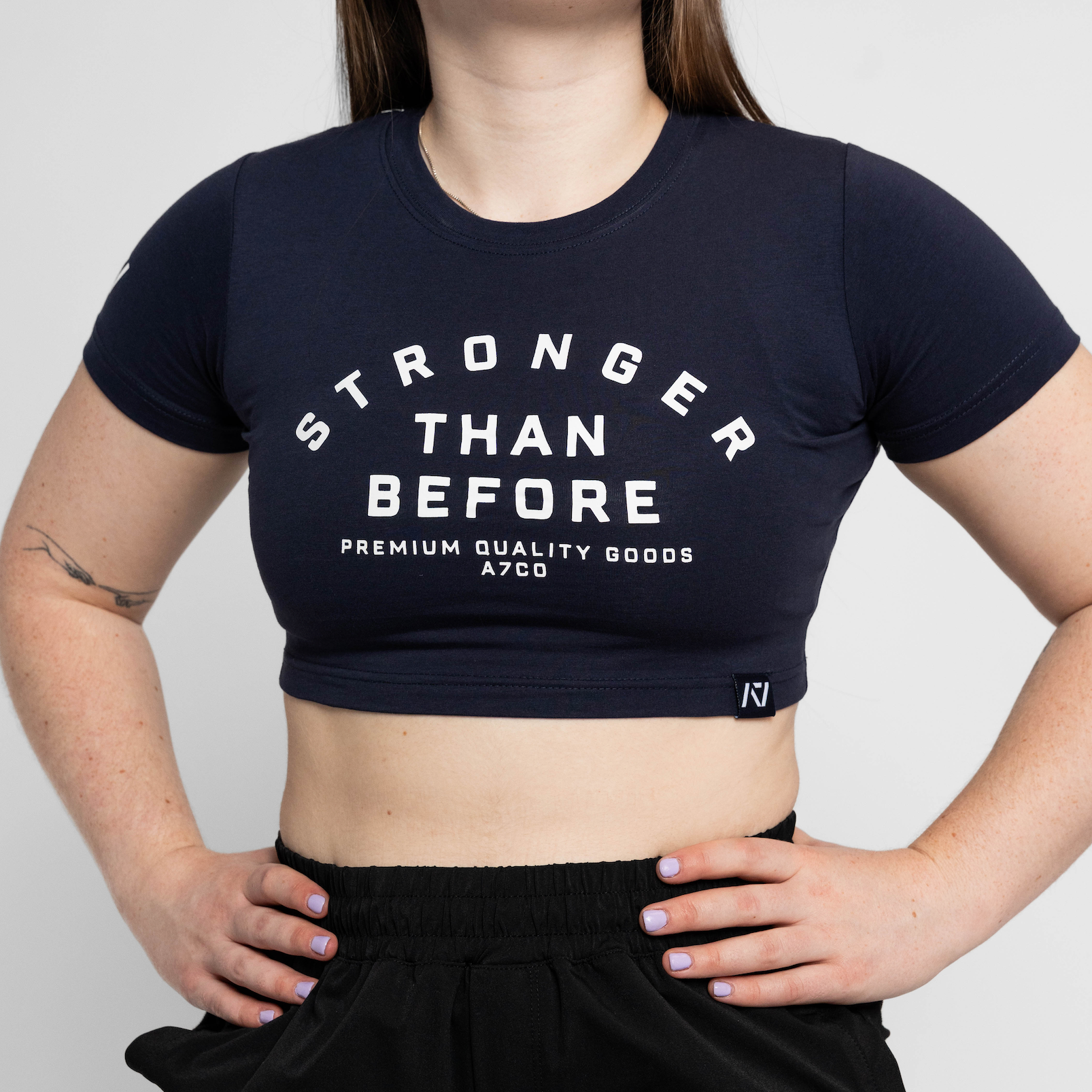 Person wearing a black crop top with 'Stronger Than Before' text on a plain background