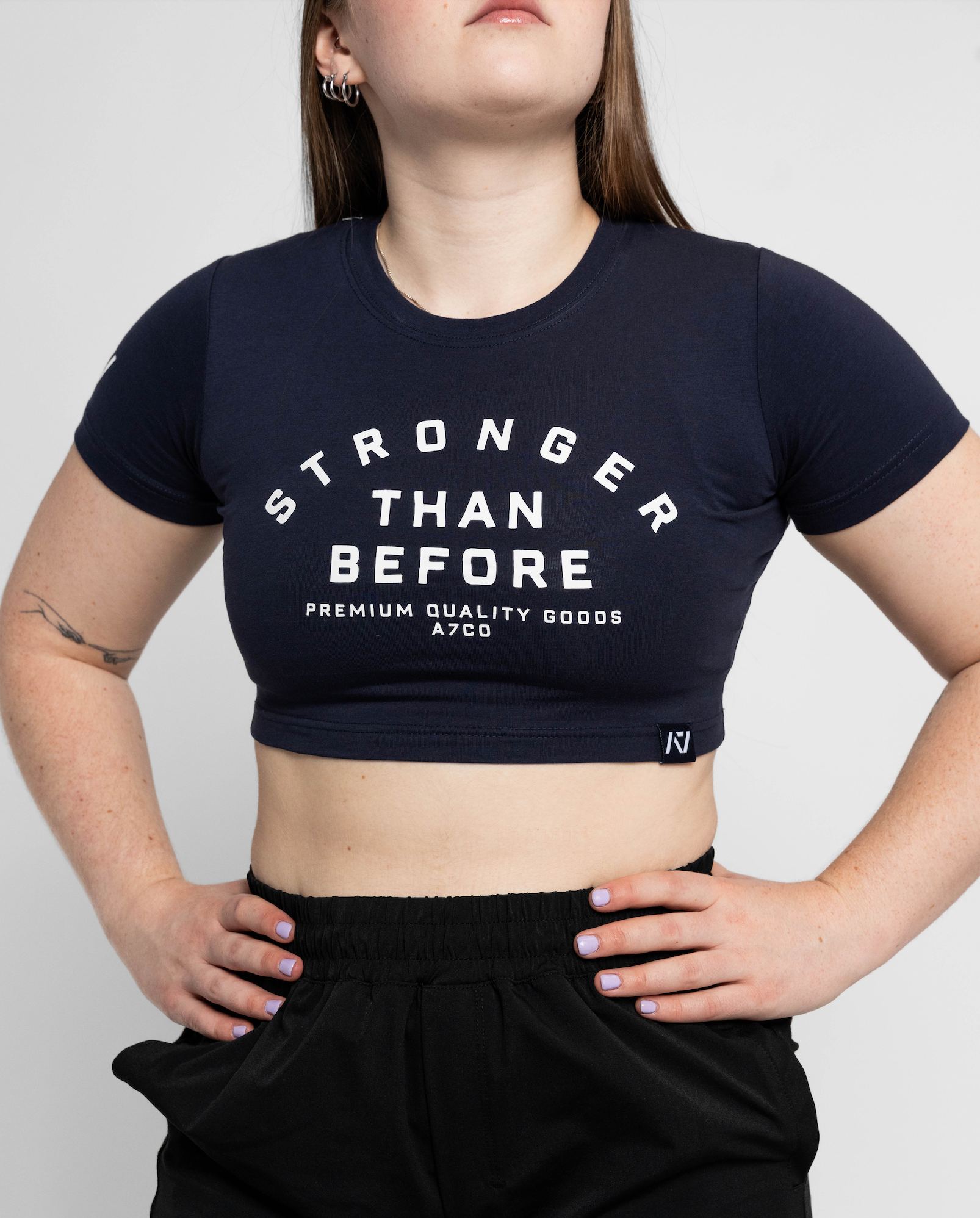 Person wearing a black crop top with 'Stronger Than Before' text on a plain background