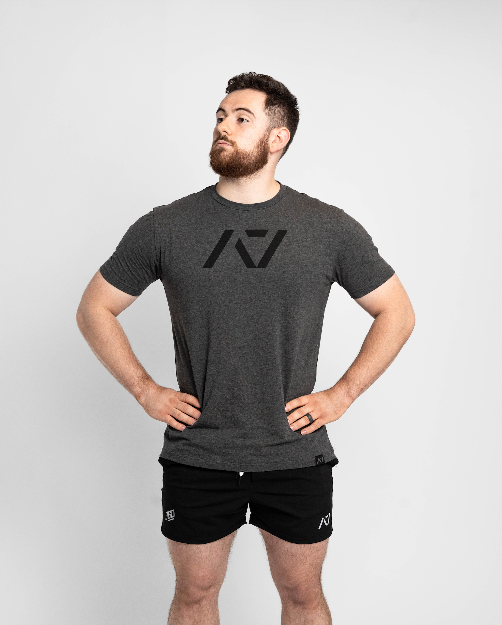 Man wearing a dark gray t-shirt and black shorts with a logo on a light gray background