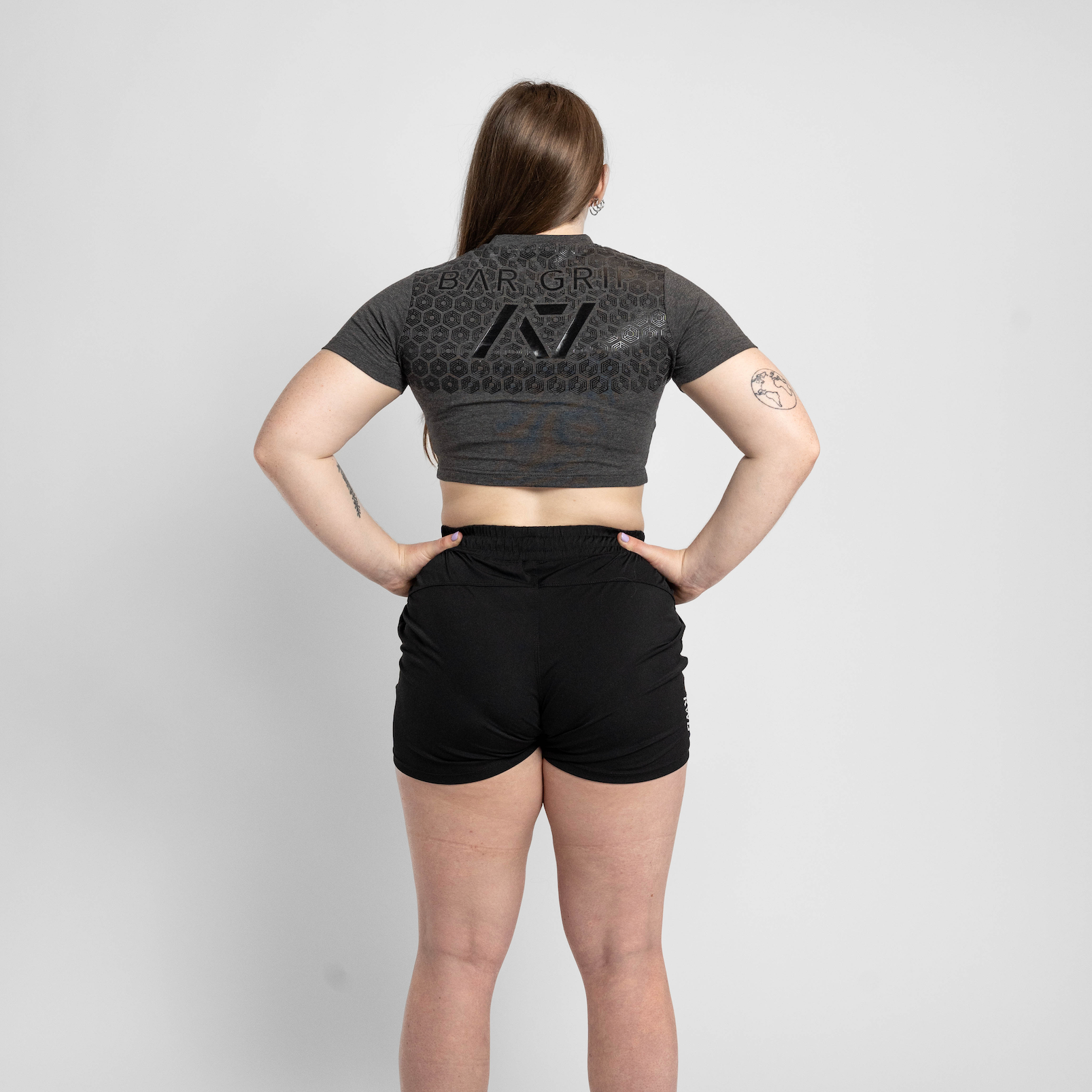 Person wearing a dark gray crop top and black shorts on a light gray background