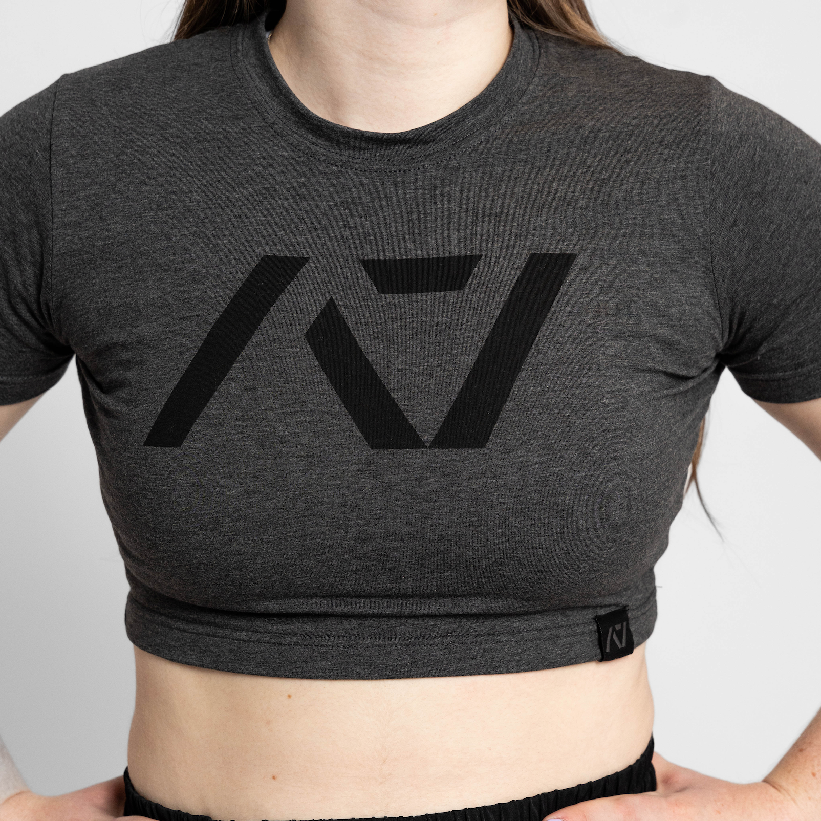 Person wearing a dark gray crop top with a logo on a plain background
