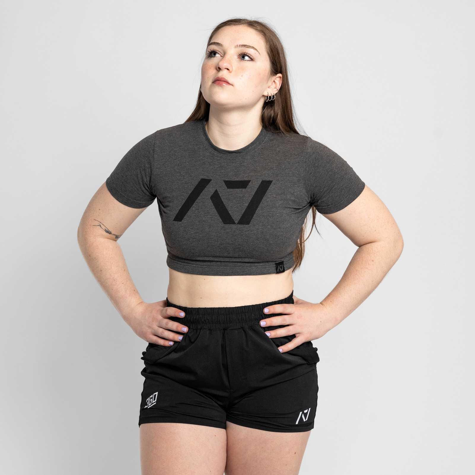 Person wearing a gray crop top with a logo and black shorts on a light gray background