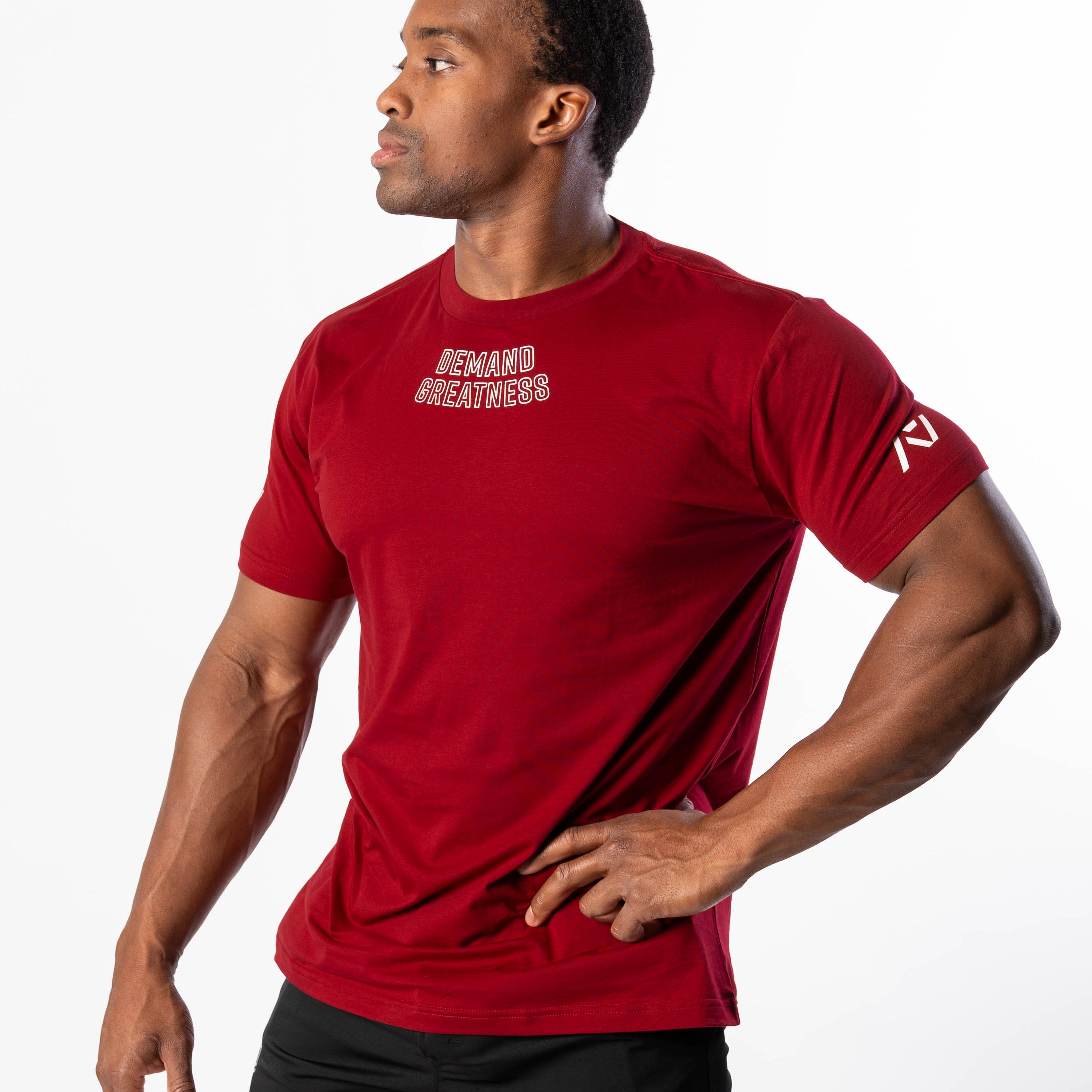 A man wearing a red Demand Greatness True-Fit men's meet shirt with a design on the upper chest and logos on the upper back and sleeves.