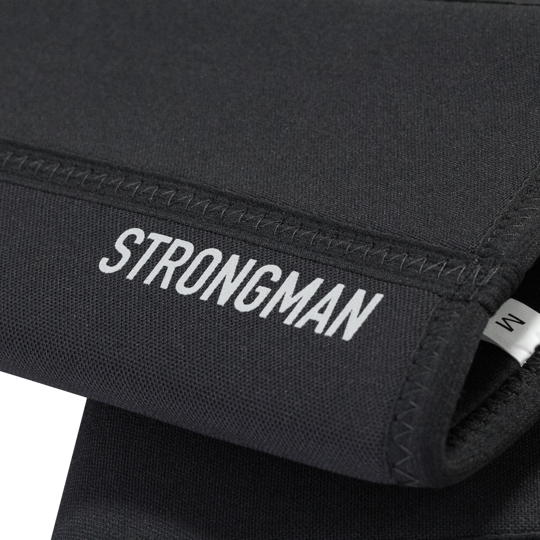 Detailed view of the reflective "Strongman" text on the black knee sleeves, emphasizing branding and design.