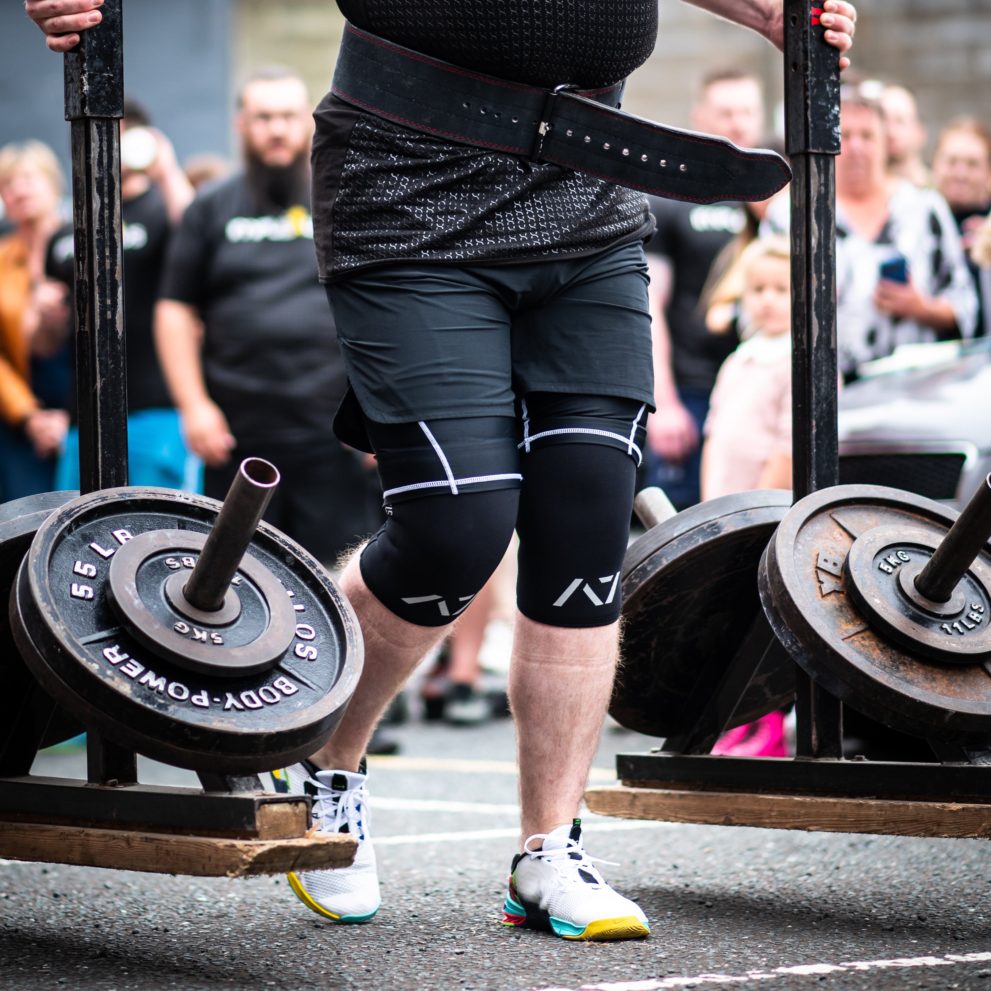 Side view of lifter executing a yoke carry with A7 Strongman Knee Sleeves – 9mm – Black/Reflective, highlighting snug fit and compression.