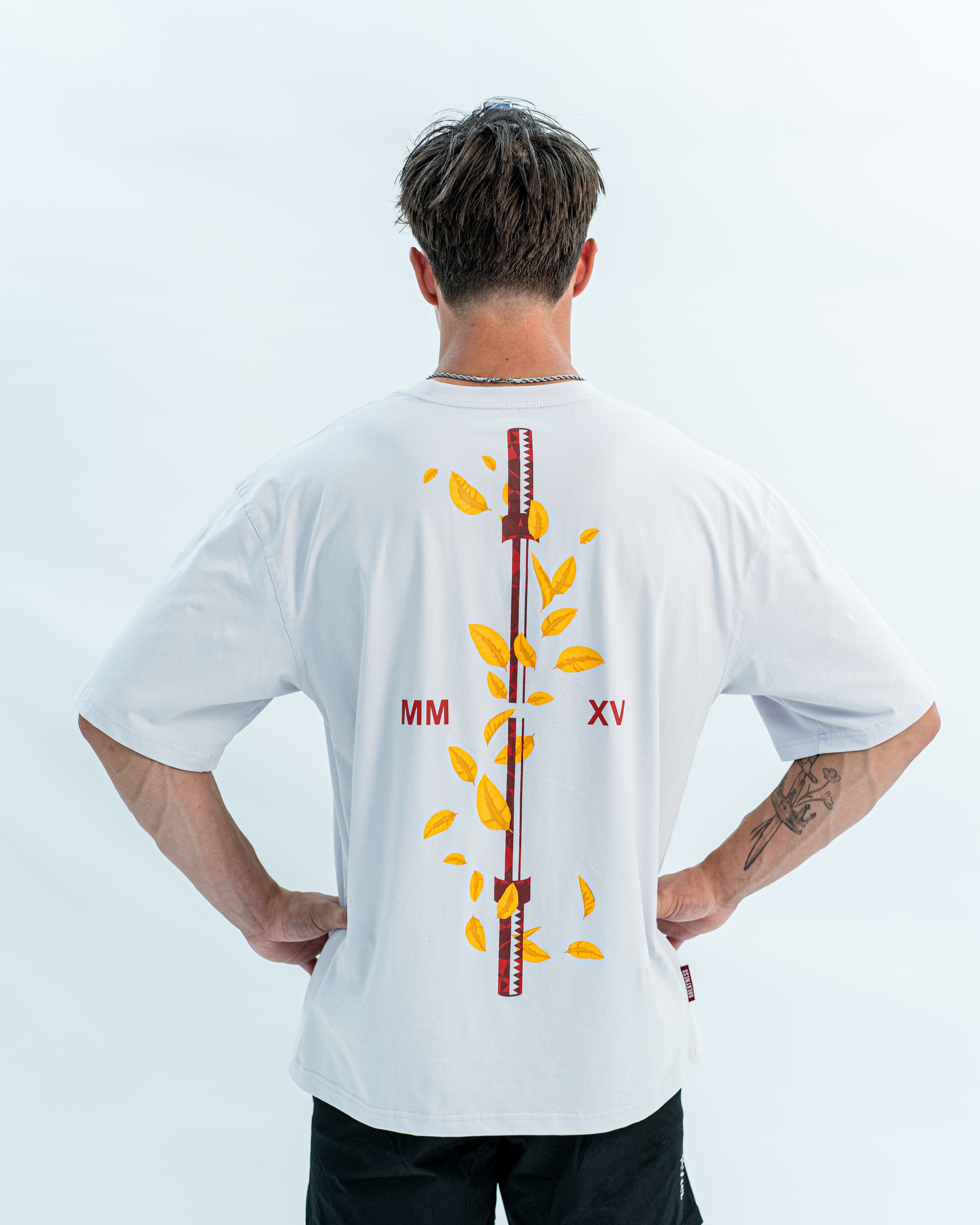 Male wearing a white over-fit shirt with a design on the back against a light gray background