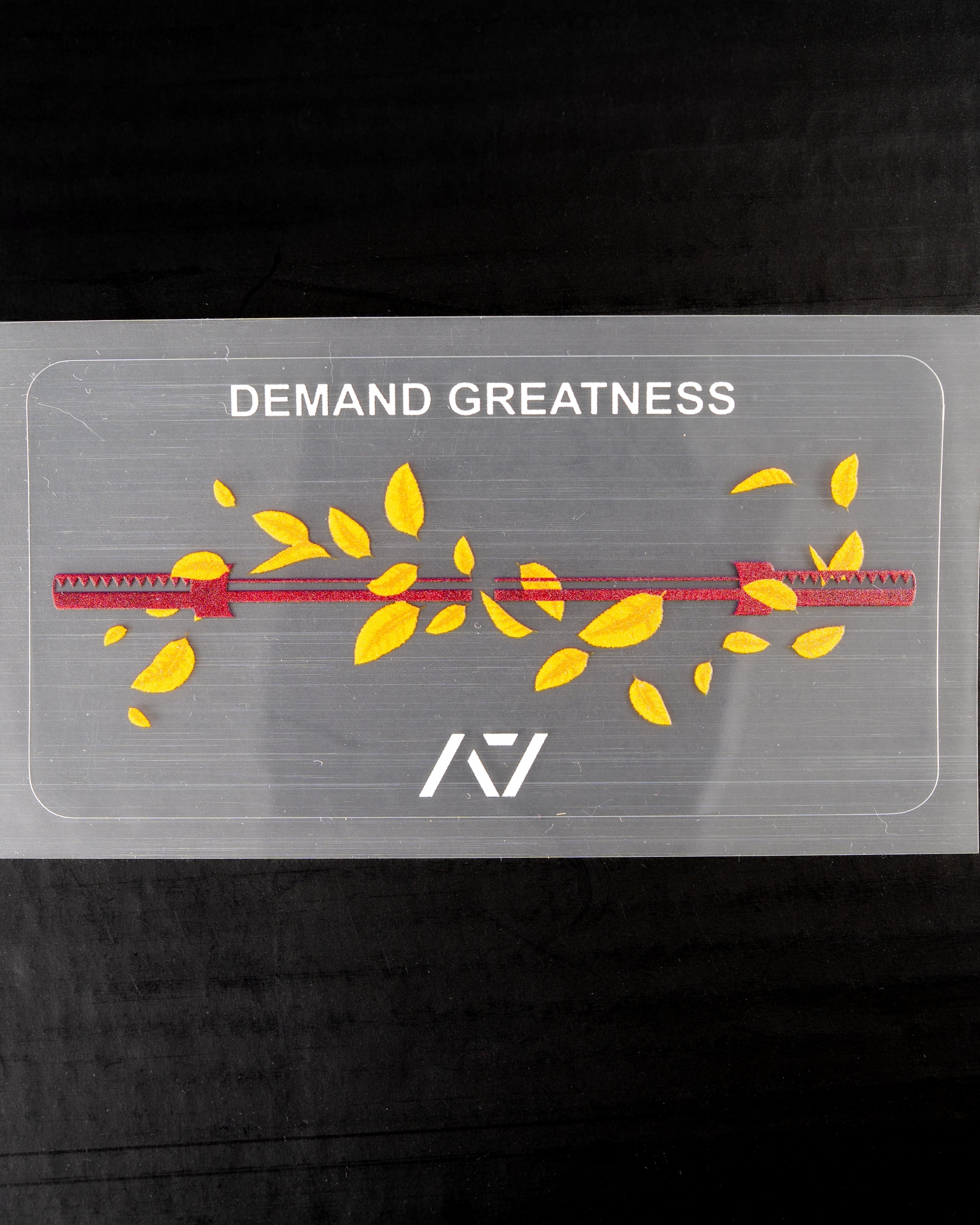 Transparent decal with 'DEMAND GREATNESS' text and yellow leaves with barbell on a black background