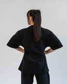 Person wearing a black outfit with wide sleeves and pants on a plain background