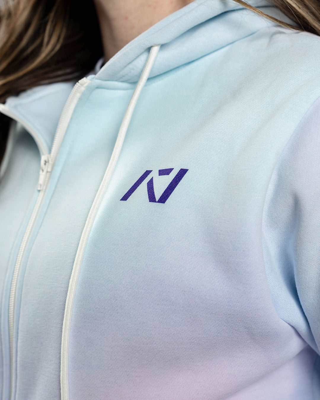 Close-up of the white A7 logo on the Affirmation Zip Hoodie – Pastel, embroidered on soft pink fabric beside a matte zipper for subtle, branded detail.