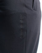 Close-up of “Demand Greatness” text printed vertically on the quad of the Stealth Defy Joggers, showcasing subtle matte branding along the leg.