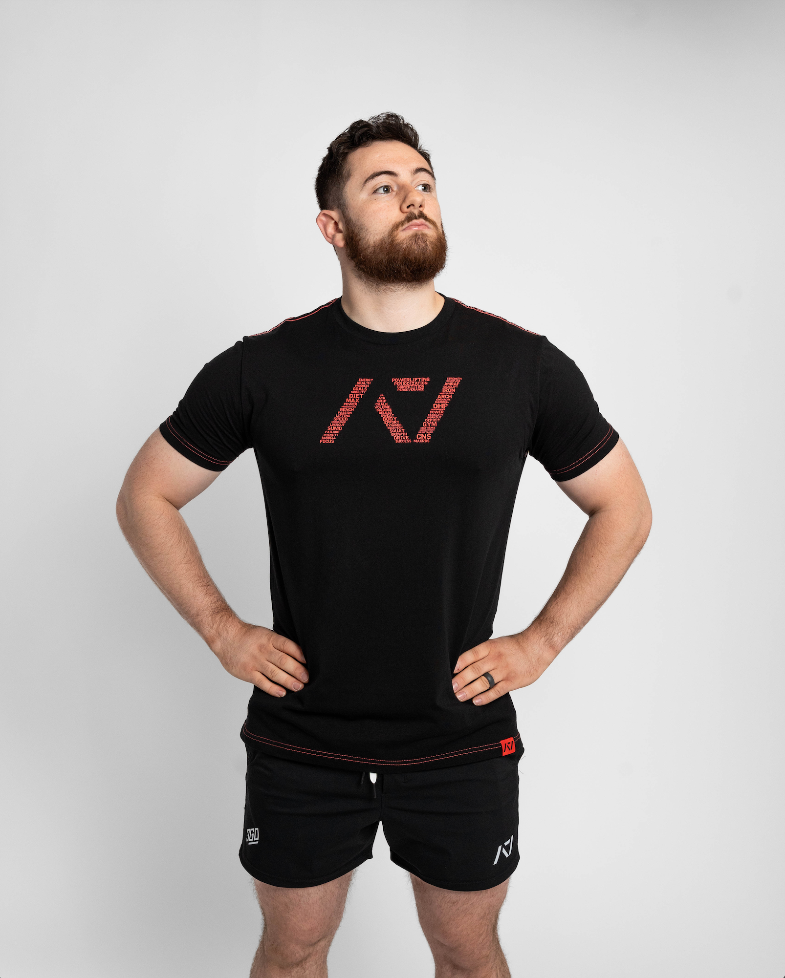 Man wearing a black t-shirt with a red logo and black shorts on a white background