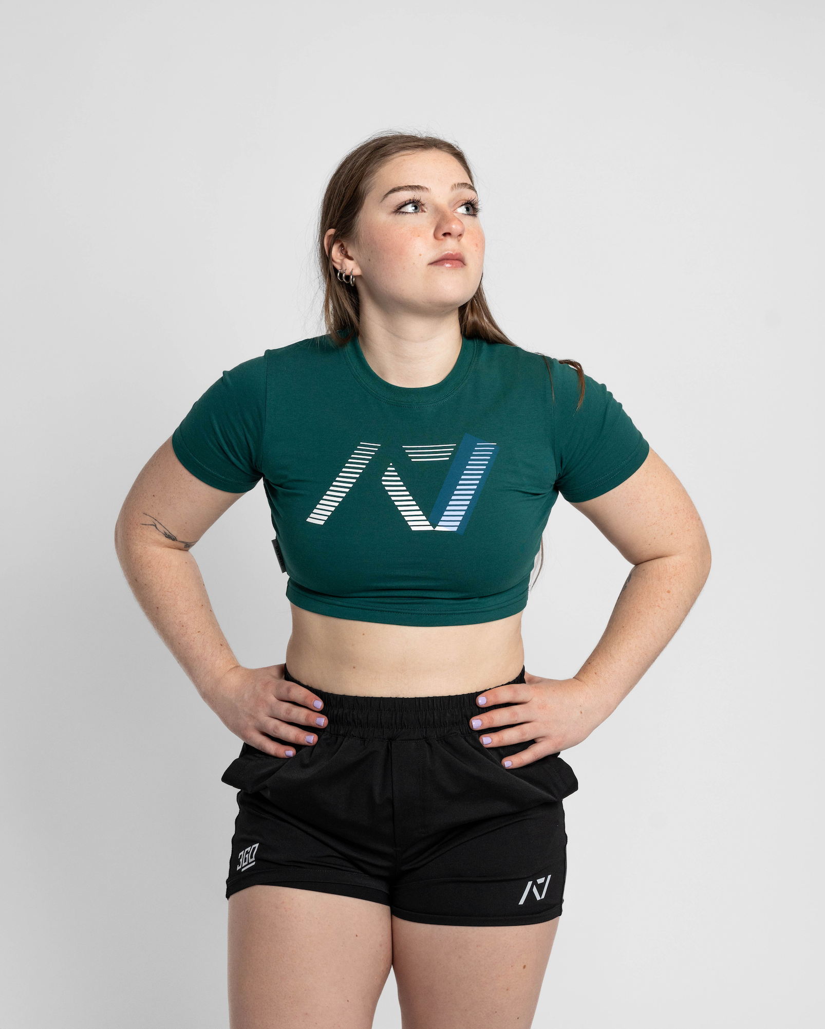 Woman wearing a green crop top and black shorts with a logo on a white background